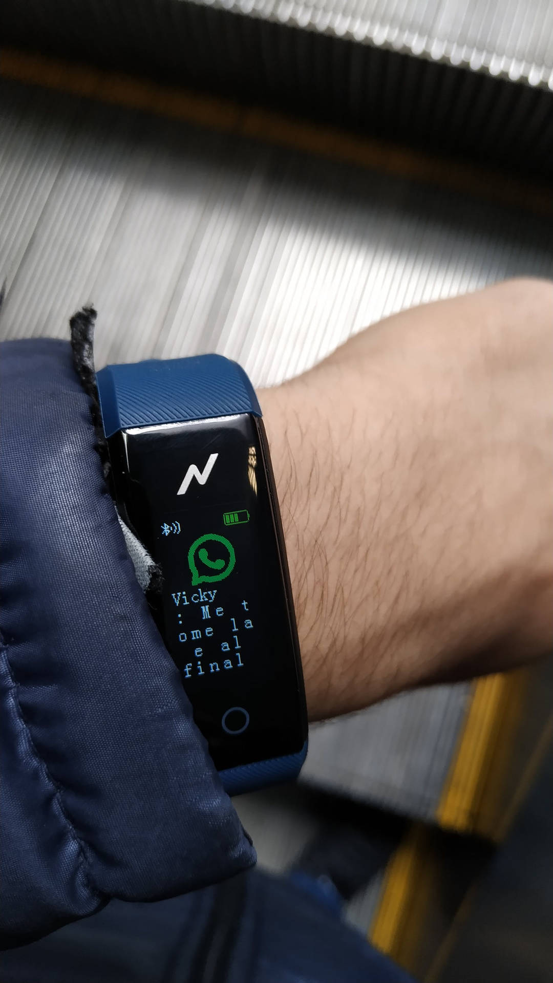 一個人的手腕戴著藍色健身追蹤器，在電扶梯上顯示 WhatsApp 訊息。 — 智慧手錶 GIF 壁紙