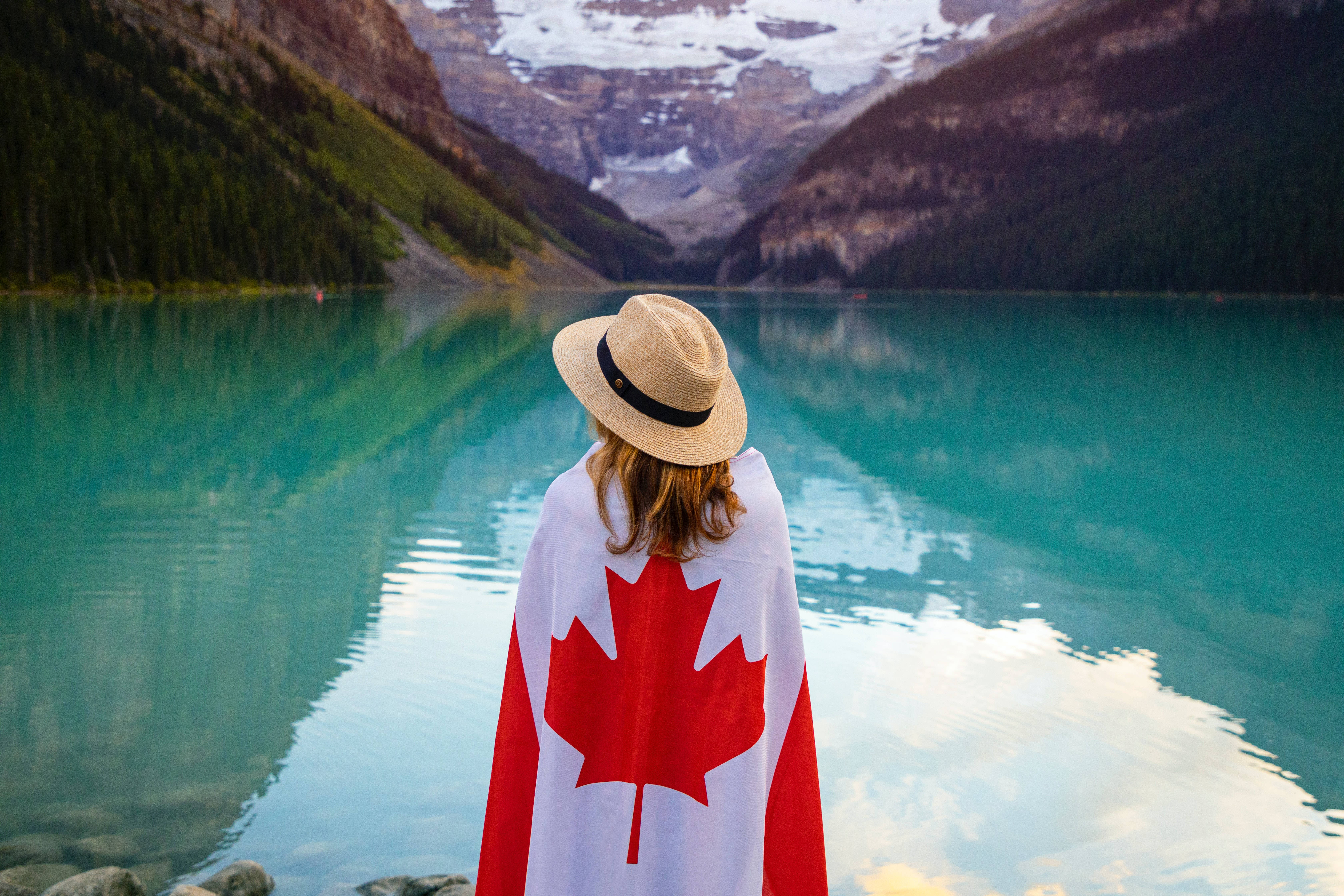 Canadian 桌布 壁紙 — 一個人披著加拿大國旗，敬畏地站在一個如鏡面般的藍綠色湖泊前，四周環繞著積雪的山峰。