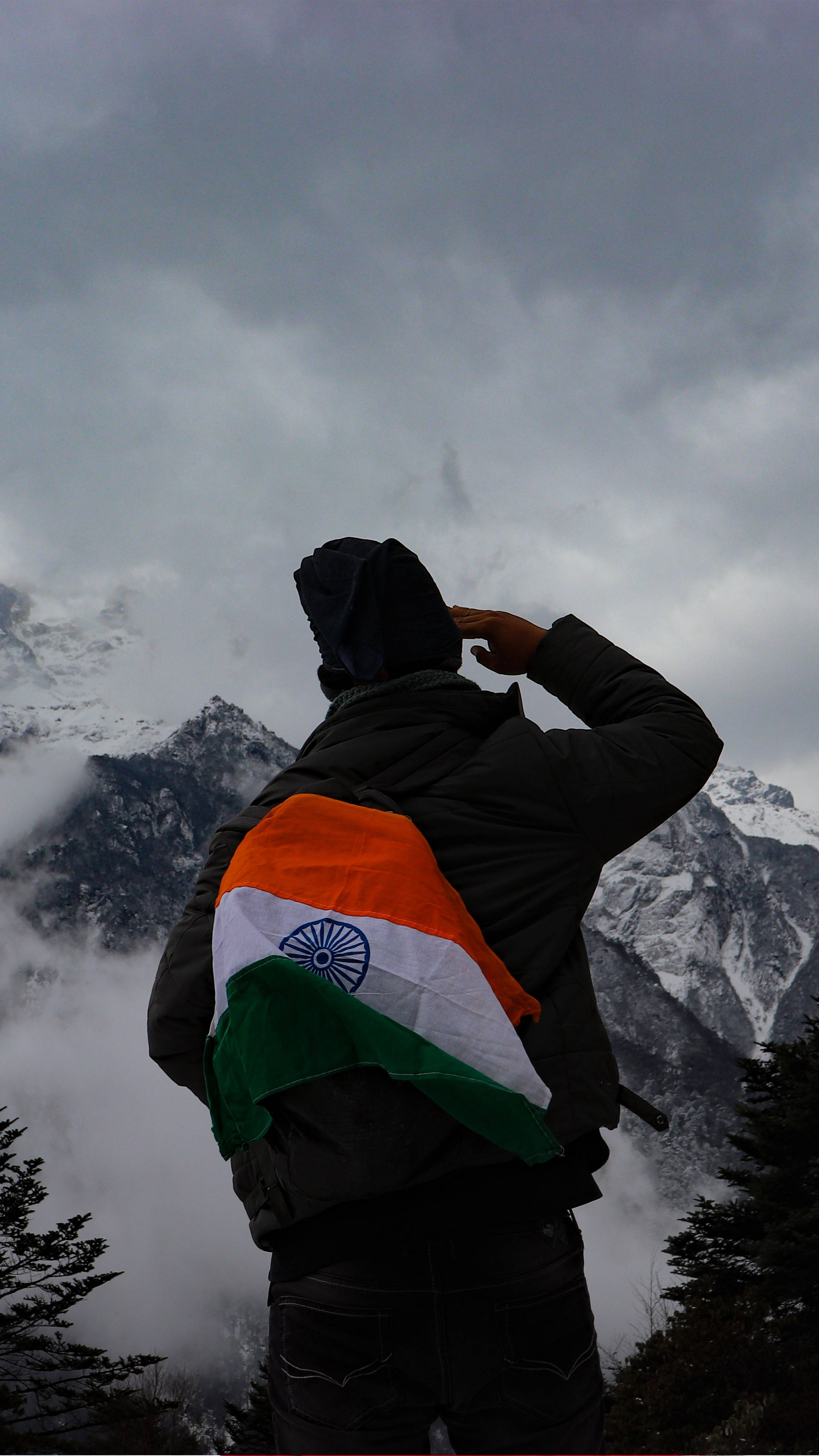 Indian 桌布 壁紙 — 一個人披著印度國旗，在白雪覆蓋的山脈和陰雲密布的天空背景下敬禮。