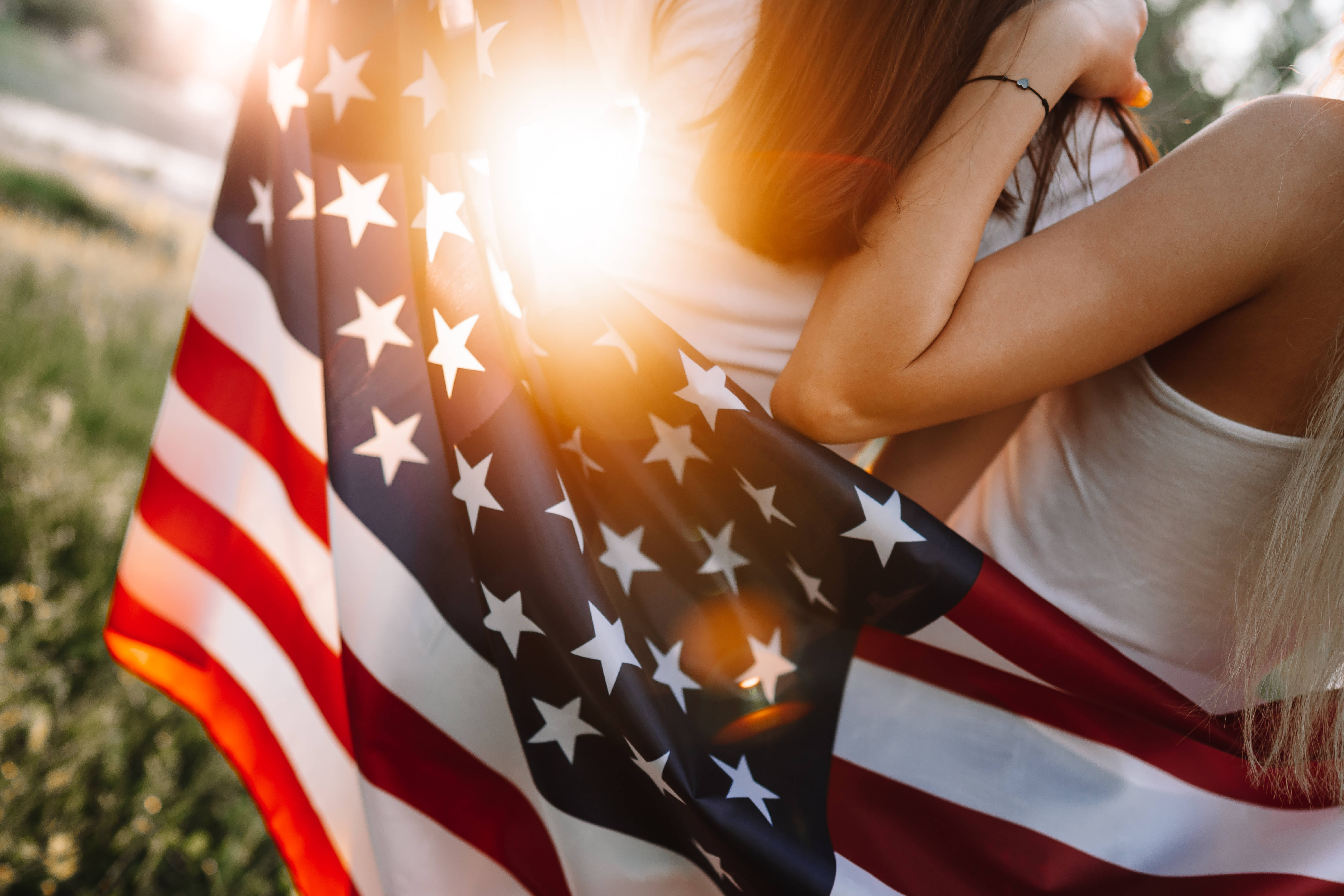 USA flag iPhone 桌布 壁紙 — 一個人披著美國國旗擁抱自己，背後有太陽耀斑發光。