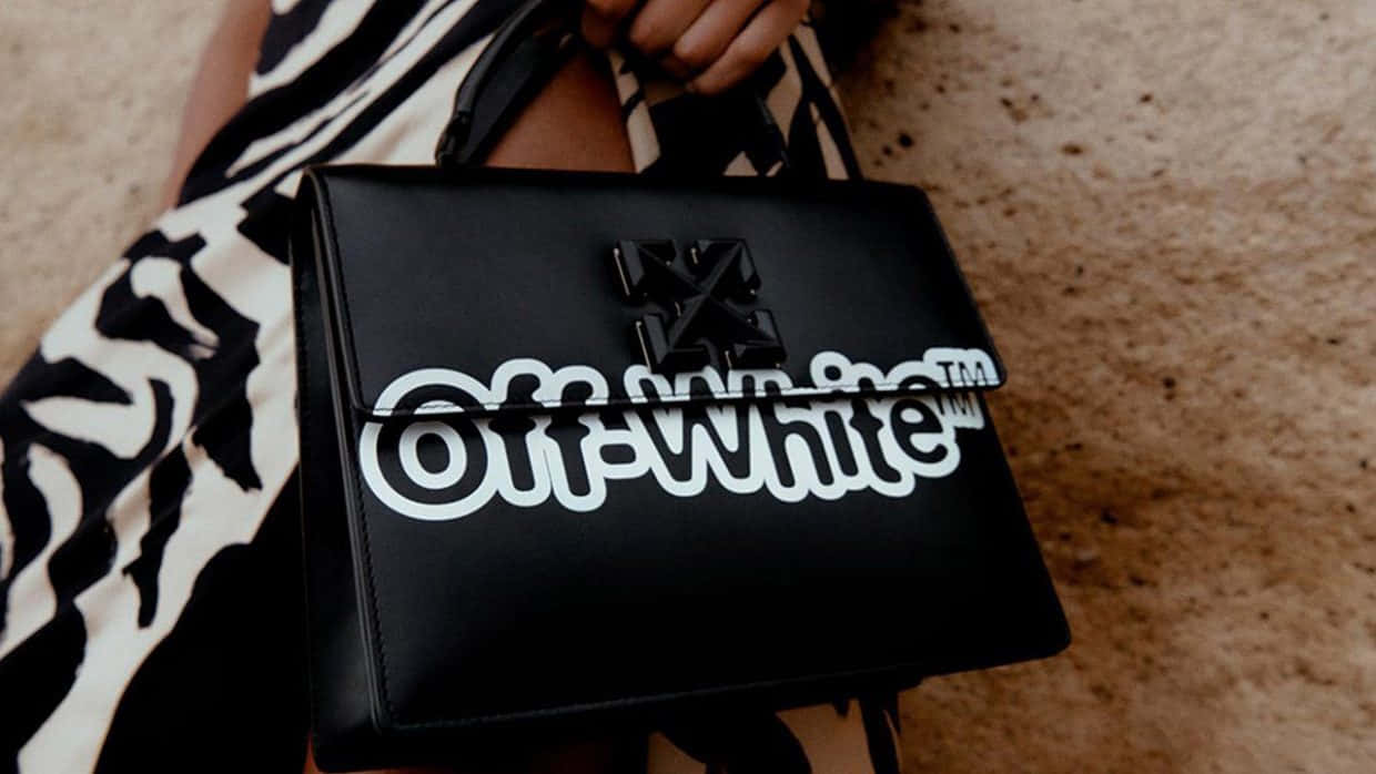 Off White 桌布 壁紙 — 一個人拿著一個黑色Off-White手袋，上面有粗體白色標誌，背景是斑馬紋連衣裙和沙地。
