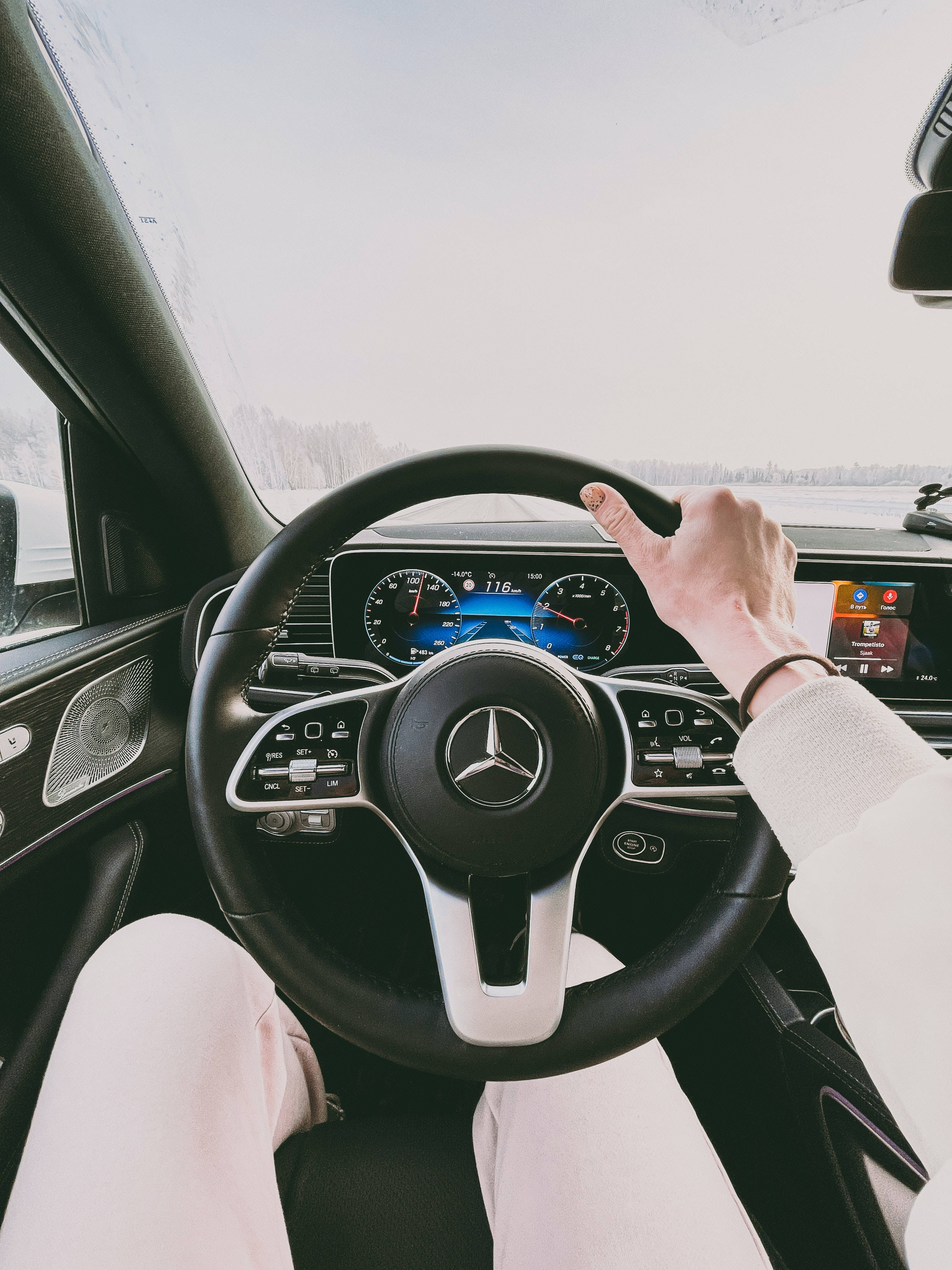 mercedes amg iPhone 桌布 壁紙 — 一個人握著一輛豪華汽車的方向盤，行駛在白雪皚皚的冬季景觀中。
