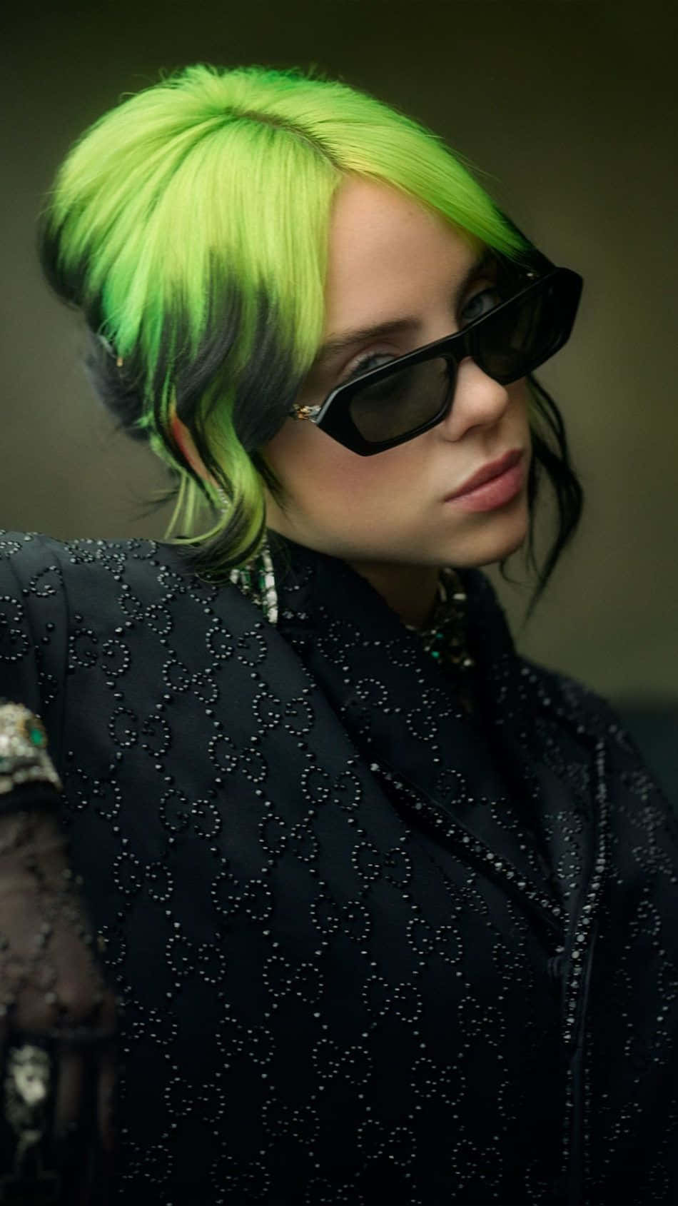 Billie Eilish 2021 桌布 壁紙 — 一個人擁有充滿活力的綠色頭髮和黑色太陽眼鏡，穿著綴有珠子的黑色外套，背景柔和。