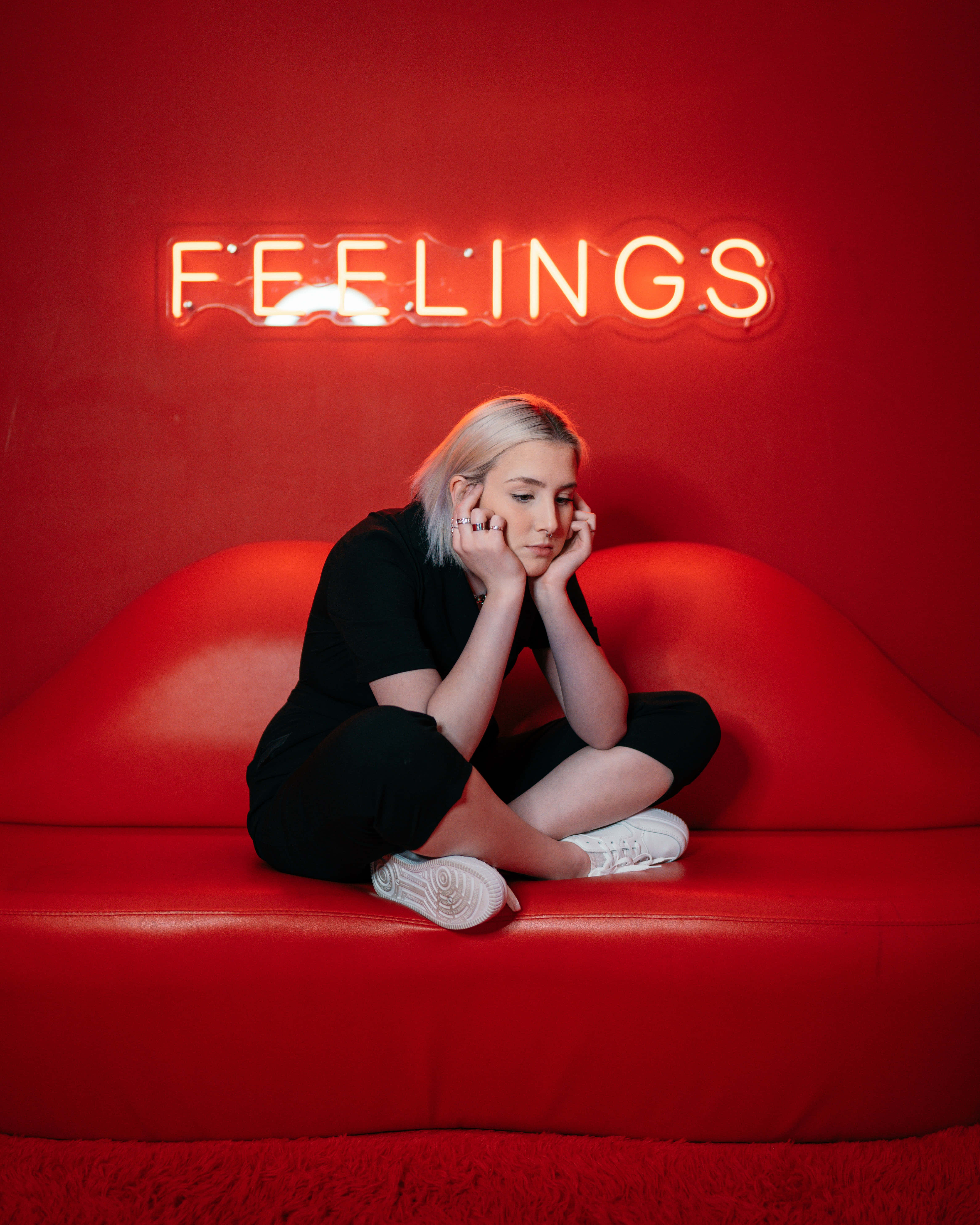 feelings 桌布 壁紙 — 一個人沉思地坐在紅色沙發上，下方是發光的紅色霓虹燈牌，寫著 FEELINGS。
