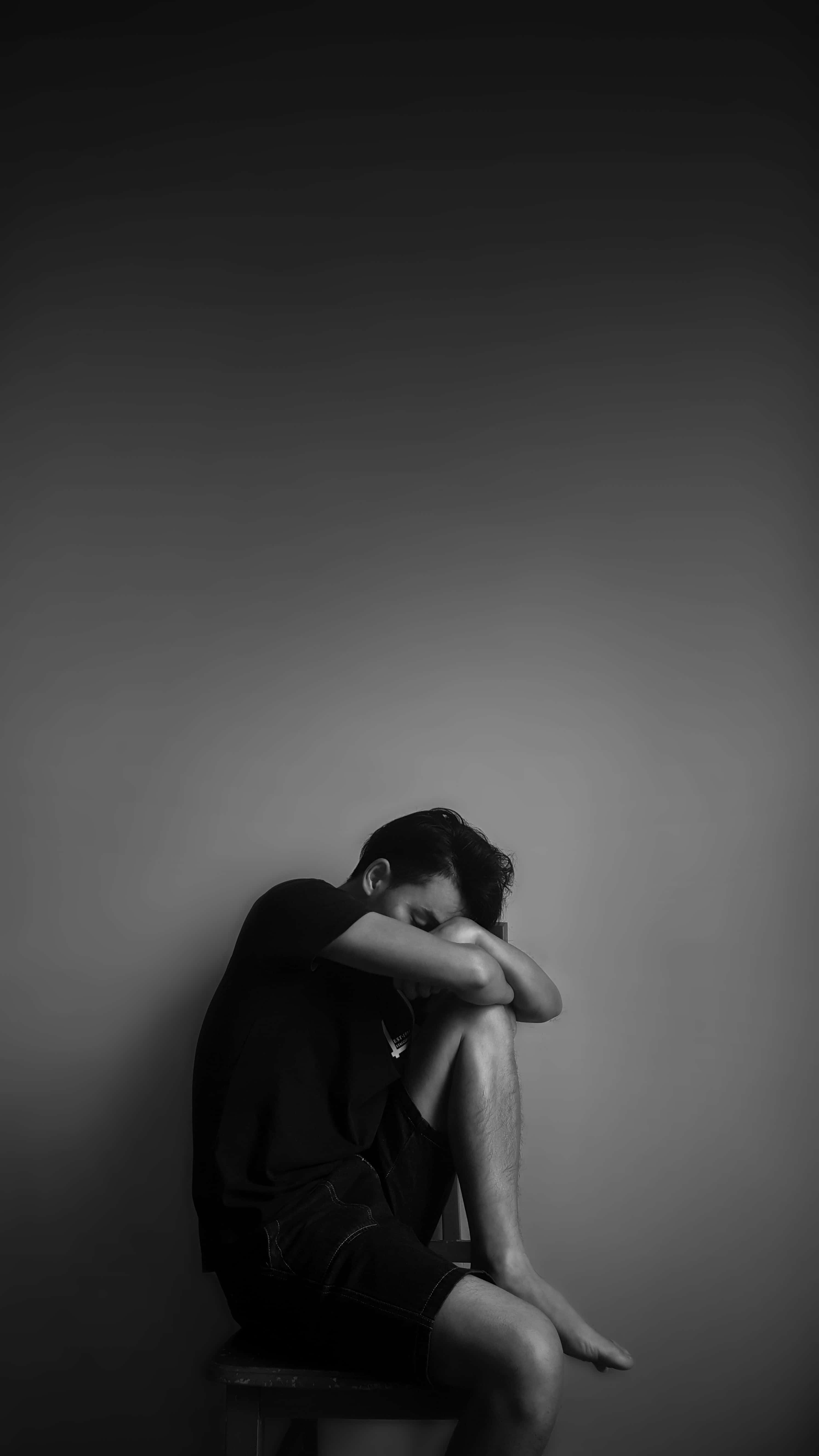 Depressed 桌布 壁紙 — 一個人獨自坐在凳子上，靠著素牆，低頭雙手抱膝，黑白肖像。