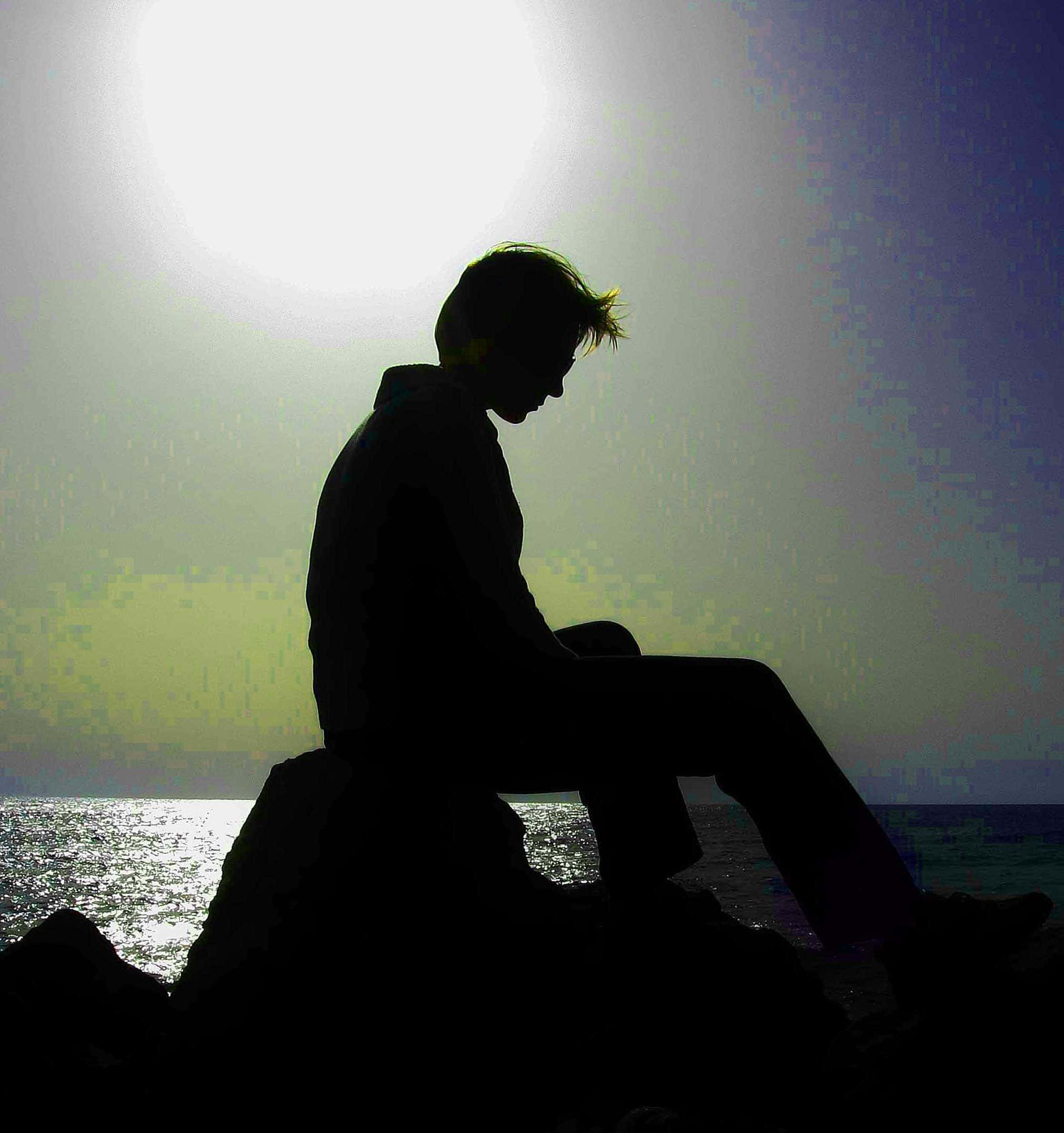 Depressing Profile 桌布 壁紙 — 一個人獨自坐在岩石海岸上，背後有明亮的夕陽，形成剪影。
