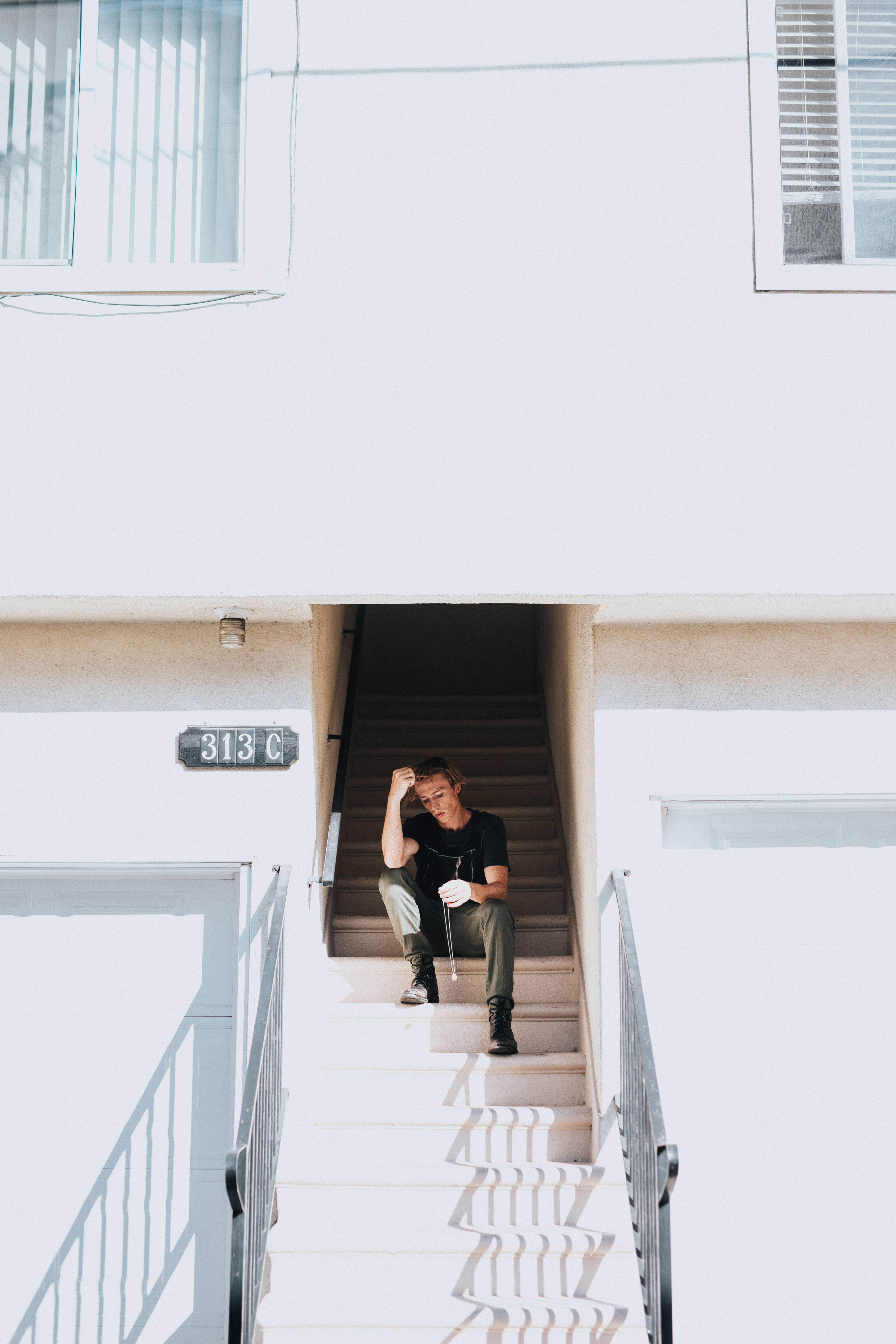 Sad Alone 桌布 壁紙 — 一個人獨自坐在明亮的白色戶外樓梯上，強烈的陽光投射出銳利的陰影。