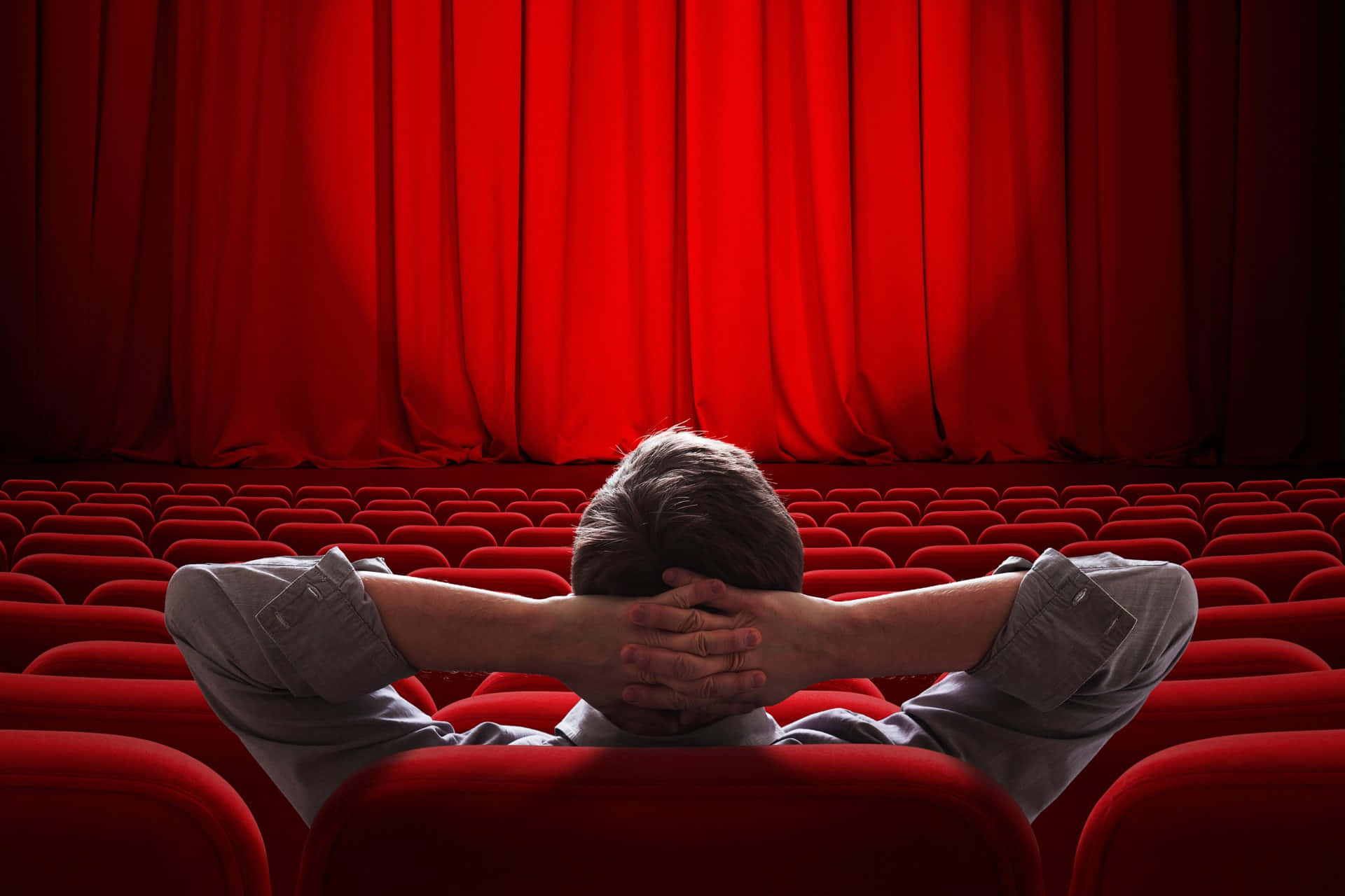 Alone 桌布 壁紙 — 一個人獨自坐在昏暗的劇院裡，雙手放在腦後，面對著一個巨大的紅色窗簾。
