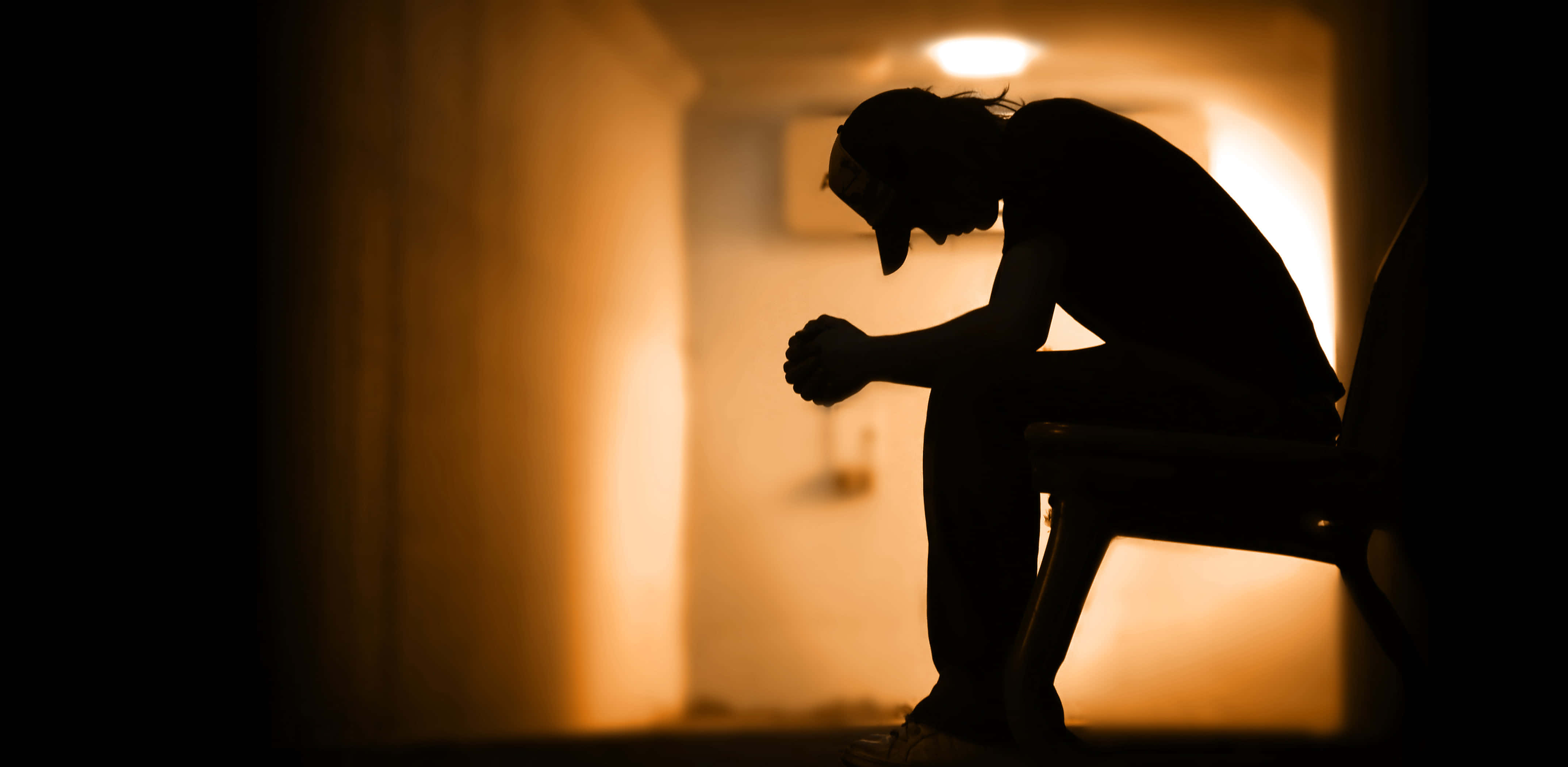 Depressed 桌布 壁紙 — 一個人獨自坐在昏暗走廊中的剪影，溫暖的背光投射出長長的影子。