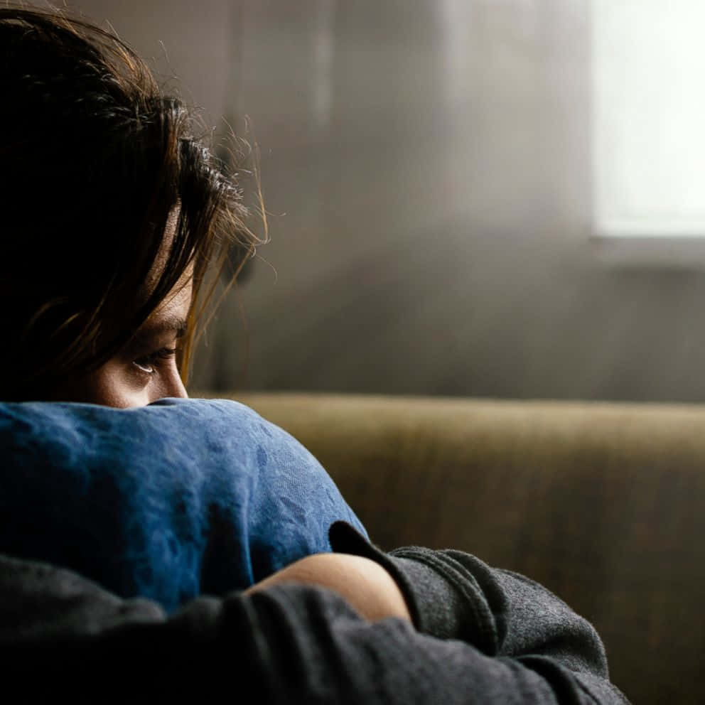 Depressed 桌布 壁紙 — 一個人獨自坐在沙發上，抱著膝蓋，房間光線昏暗，窗戶透進柔和自然光。