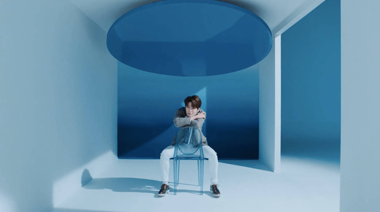 Blue Aesthetic Desktop 桌布 壁紙 — 一個人獨自坐在透明椅子上，身處一個極簡藍色房間，頭頂有一個大型圓形天窗。
