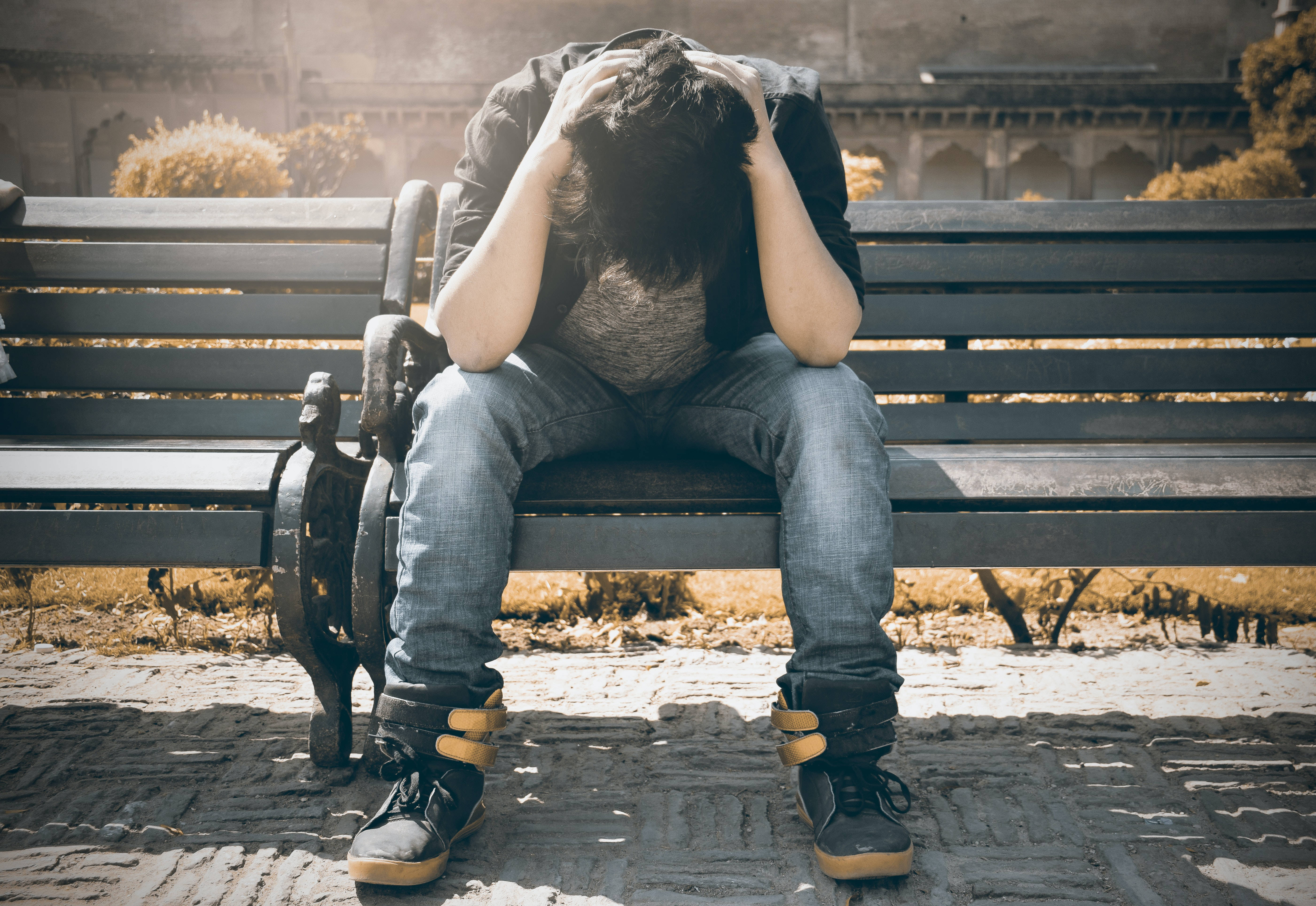 mood 桌布 壁紙 — 一個人癱坐在公園長椅上，在溫暖陽光下將頭埋在雙手中。