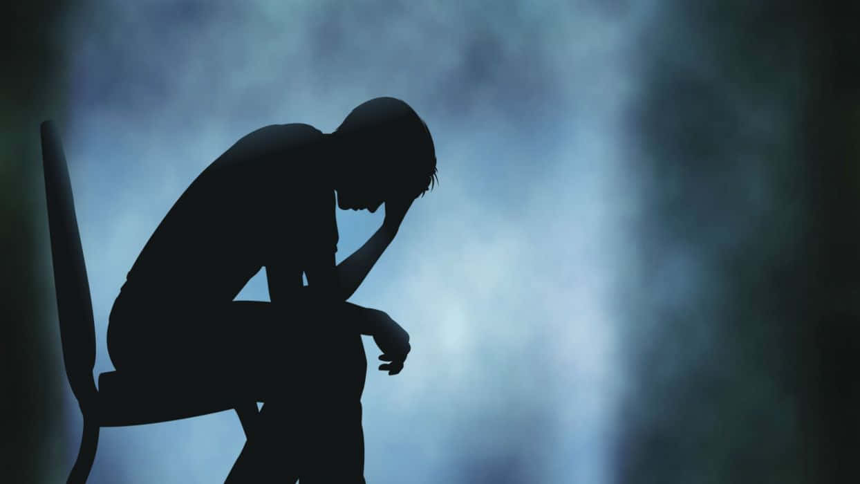 Silhouette 桌布 壁紙 — 一個人癱坐在椅子上，頭枕著手，以剪影形式呈現，背景是憂鬱的藍色漸變。