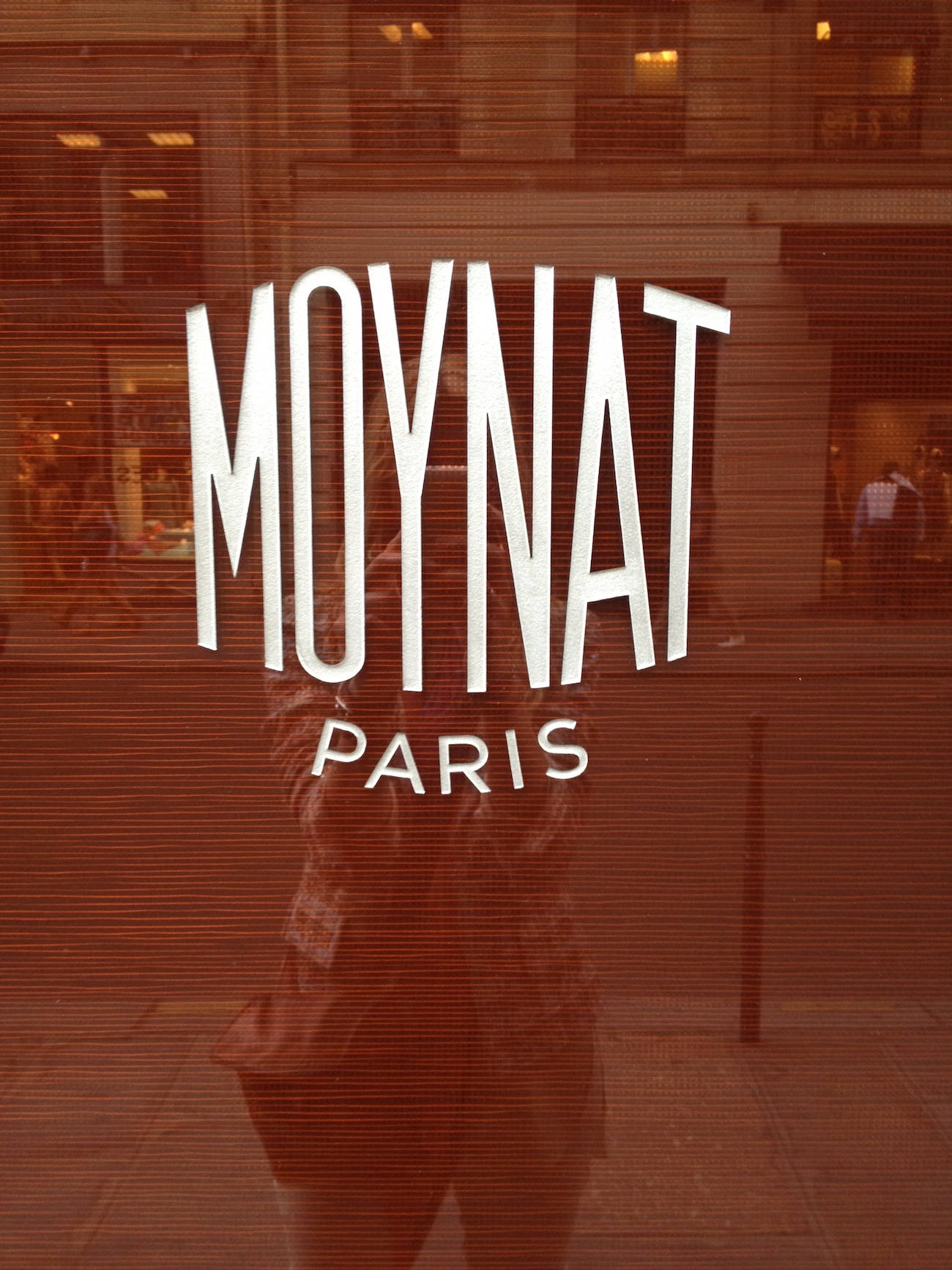 Designer Logo 桌布 壁紙 — 一個人的倒影和「MOYNAT PARIS」標誌在有色玻璃商店櫥窗上可見，水平百葉窗投射出條紋。