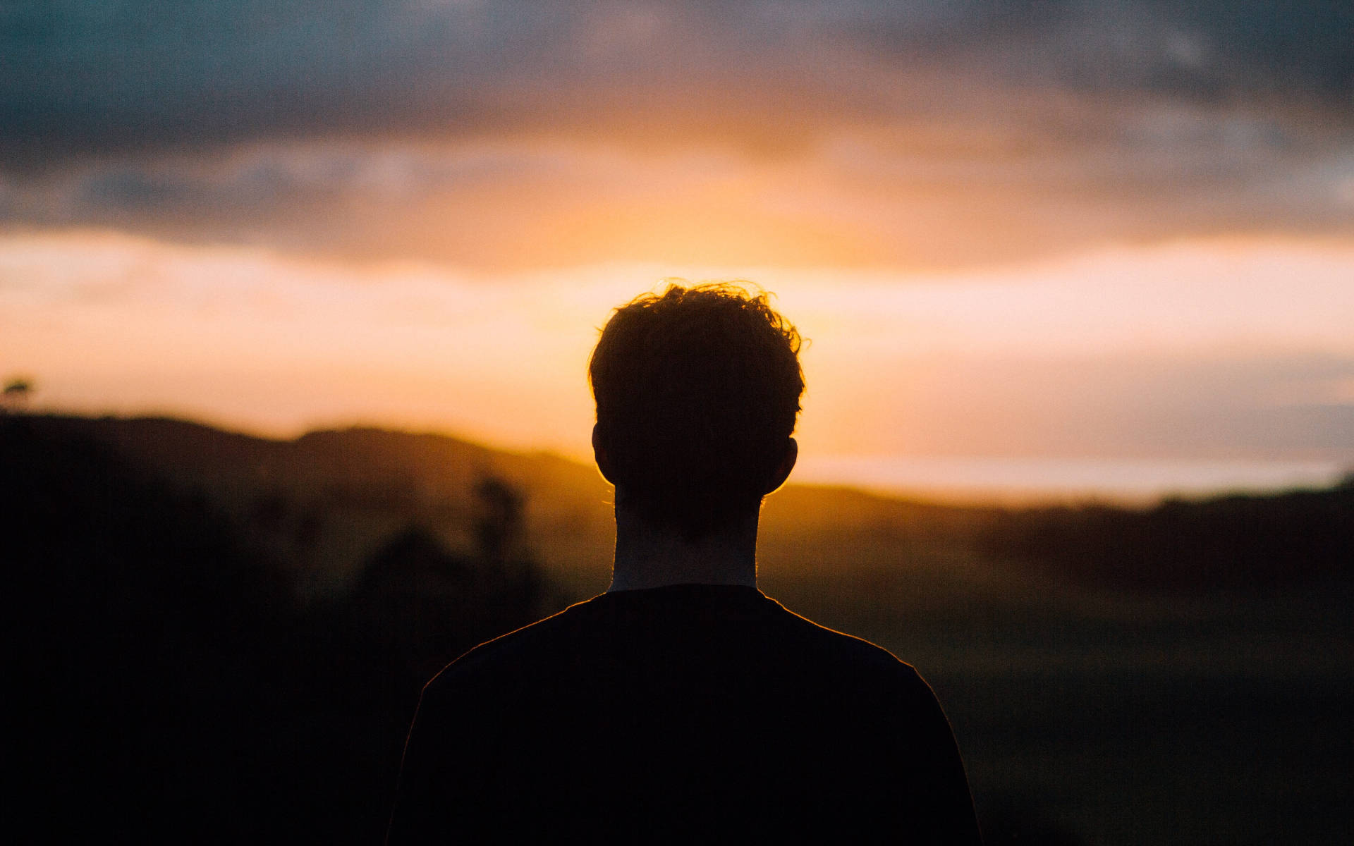 Alone 桌布 壁紙 — 一個人的剪影，凝視著連綿山丘上充滿活力的橙色和粉紅色日落。