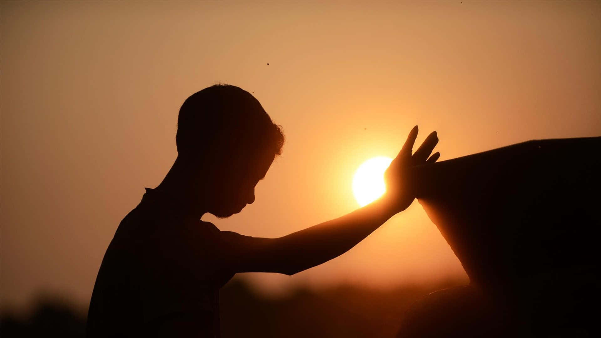 Praying 桌布 壁紙 — 一個人的剪影，在日落時分伸出手朝向太陽，背景是溫暖的橙色天空。