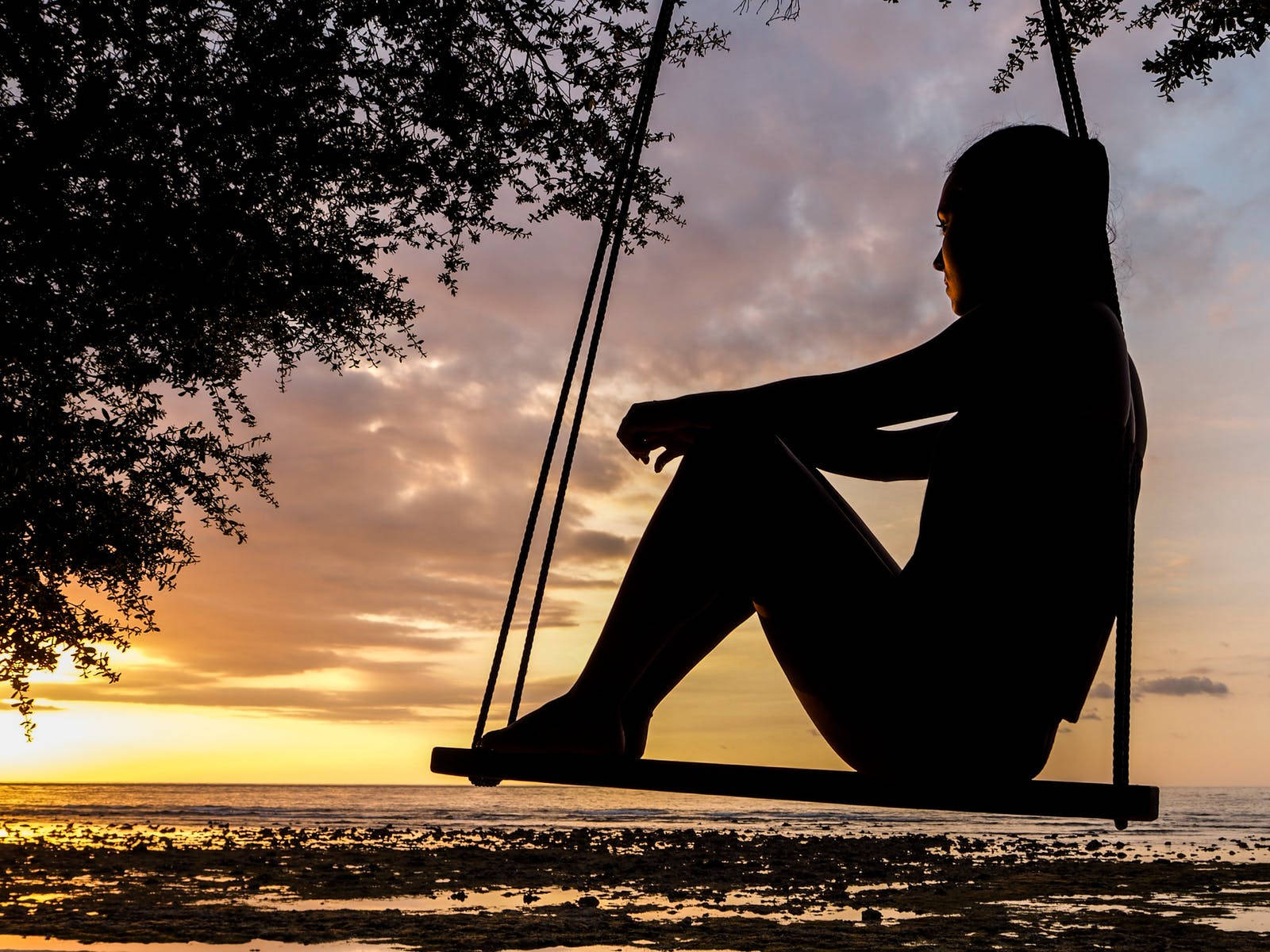 Relaxing 桌布 壁紙 — 一個人的剪影，坐在鞦韆上，日落時分俯瞰海洋，頭頂有樹枝。