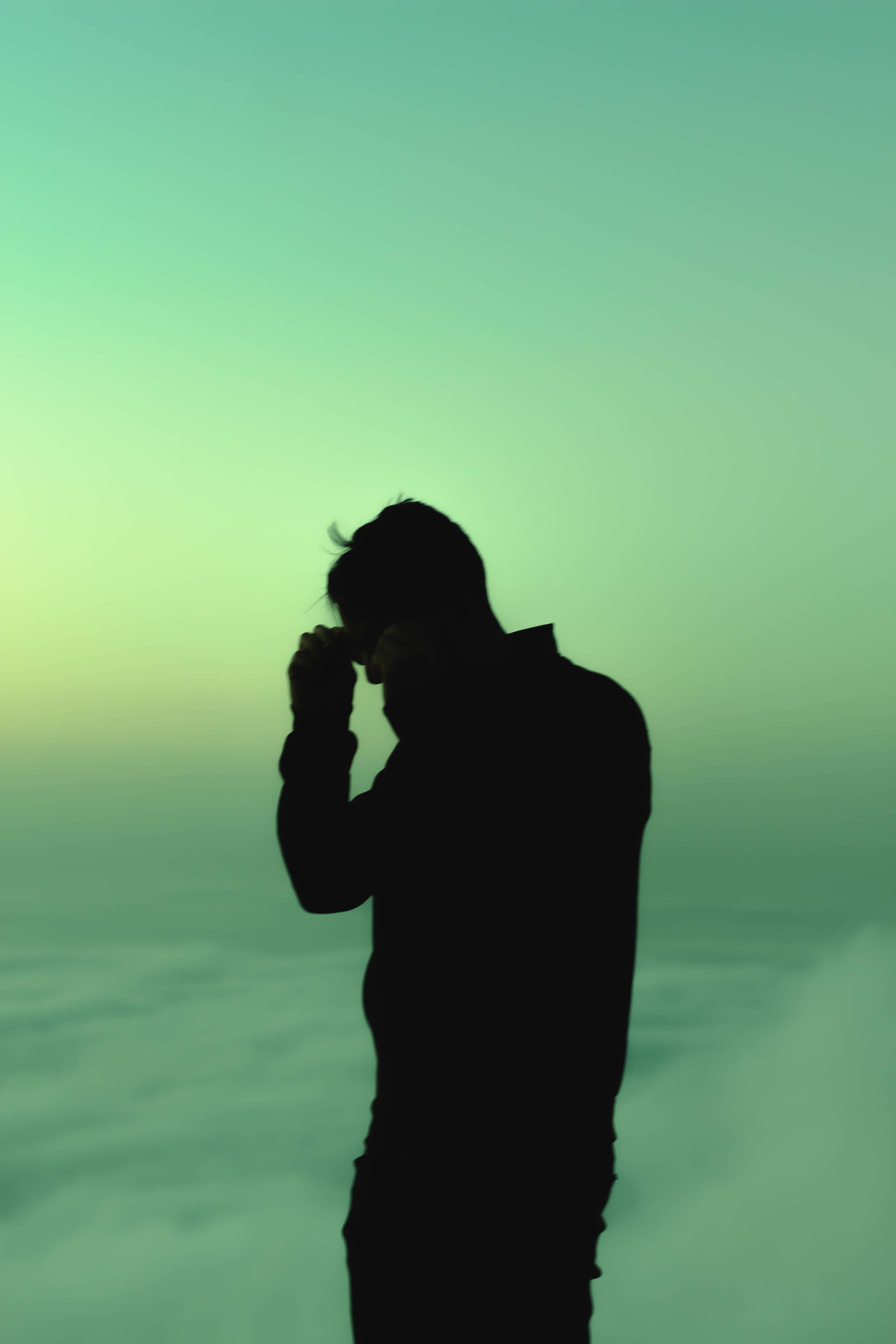 popular phone 桌布 壁紙 — 一個人的剪影，站在雲層之上，雙手靠近臉部，背景是漸變的綠色天空。