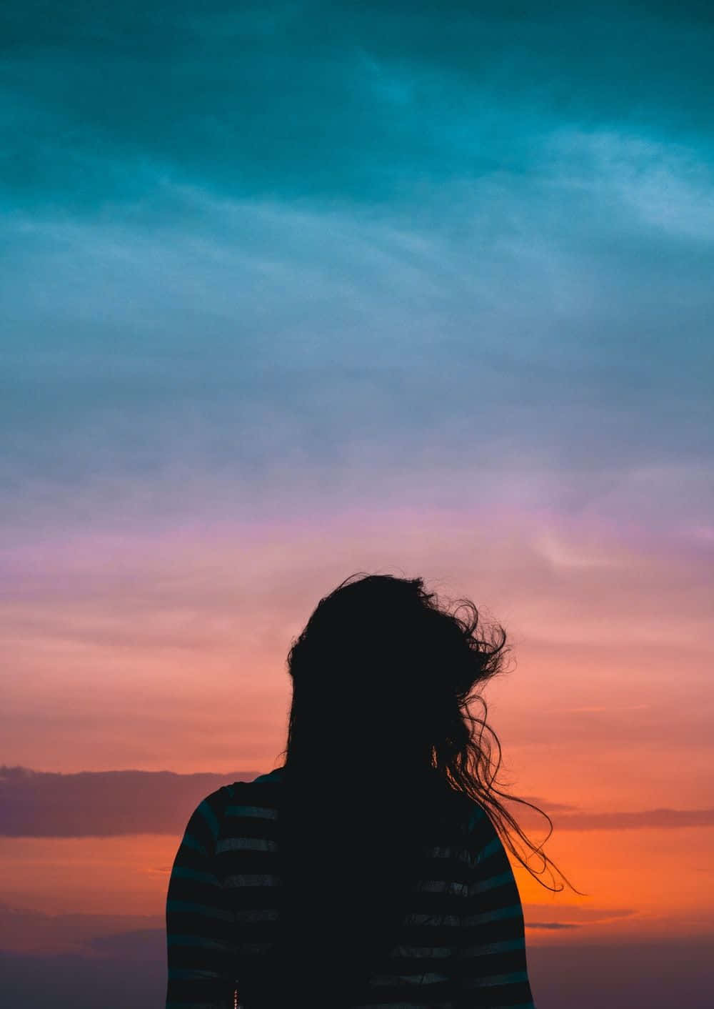 Silhouette 桌布 壁紙 — 一個人的剪影，頭髮被風吹起，背景是充滿活力的暮色天空，融合了青綠色、粉紅色和橙色的色調。