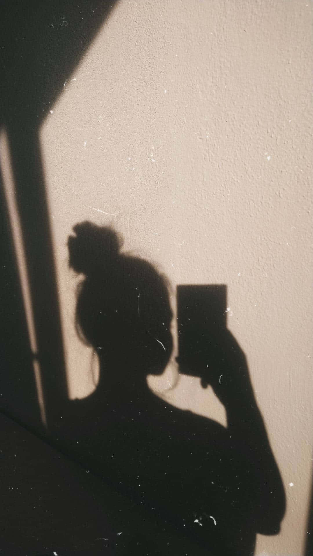 shadow 桌布 壁紙 — 一個人的剪影在紋理牆壁上投下深色陰影，同時舉起手機捕捉自己的倒影。