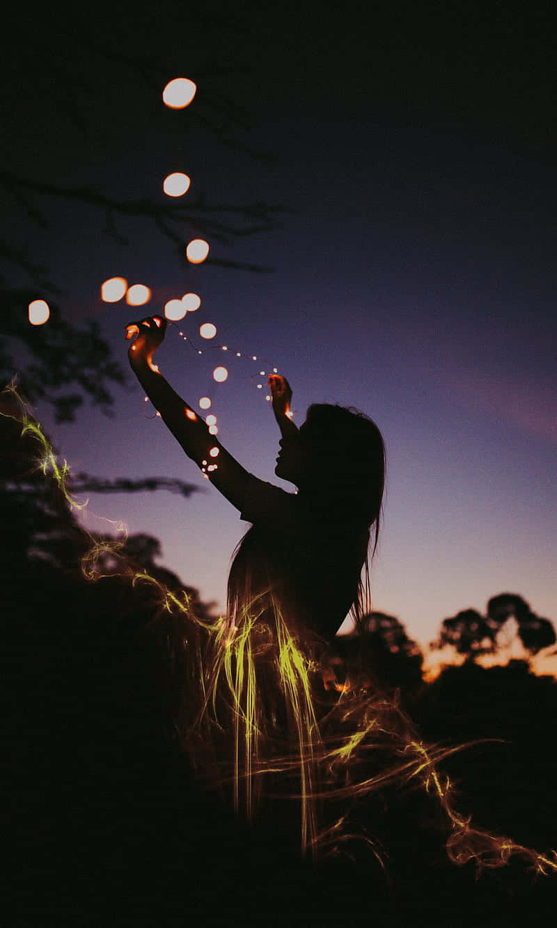 Silhouette 桌布 壁紙 — 一個人的剪影在黃昏時將發光的球體釋放到暮色天空中，樹枝框住了場景。