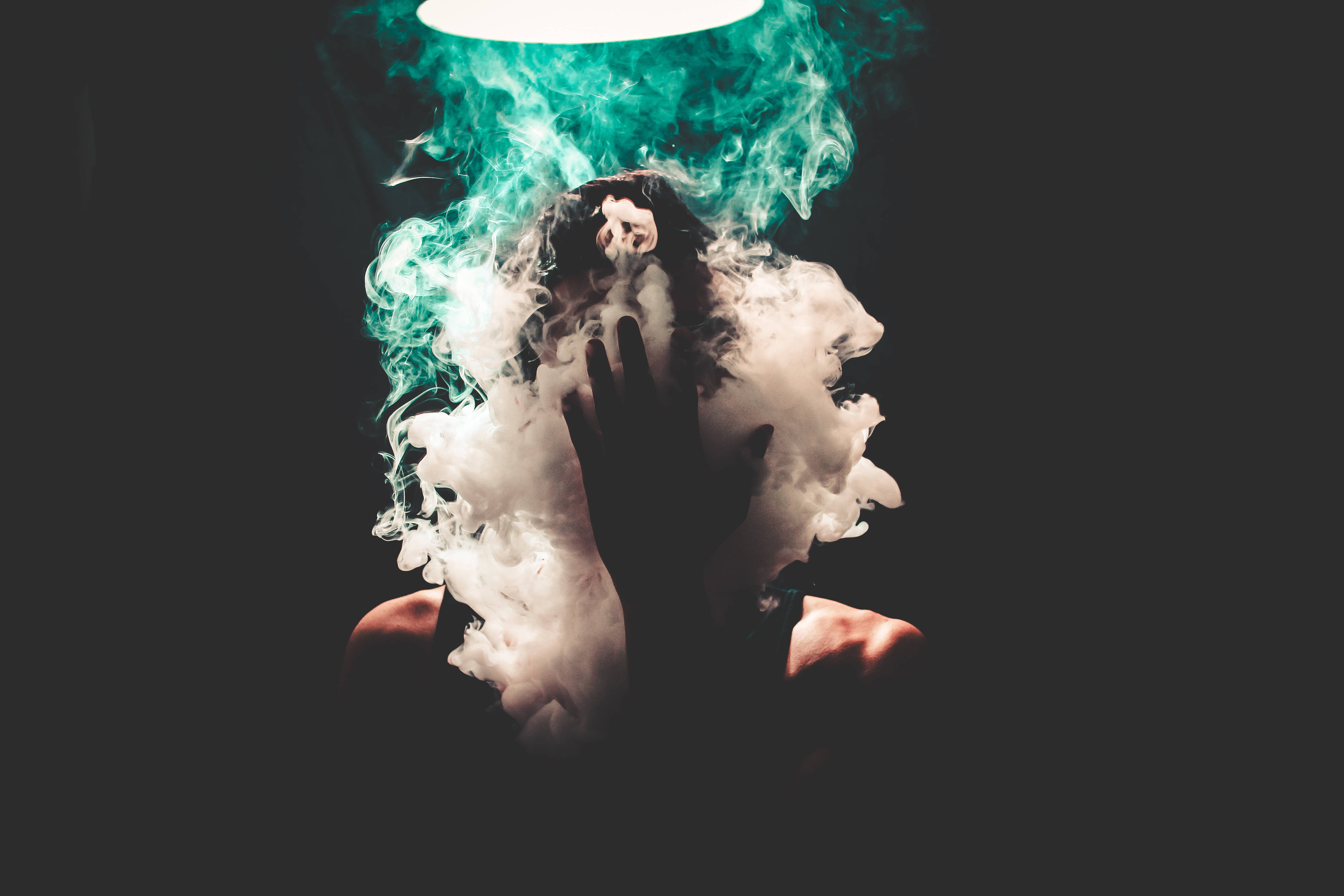 No Face 桌布 壁紙 — 一個人的剪影從旋轉的白色和藍綠色煙霧中浮現，在黑色背景下有一圈發光的圓形光。