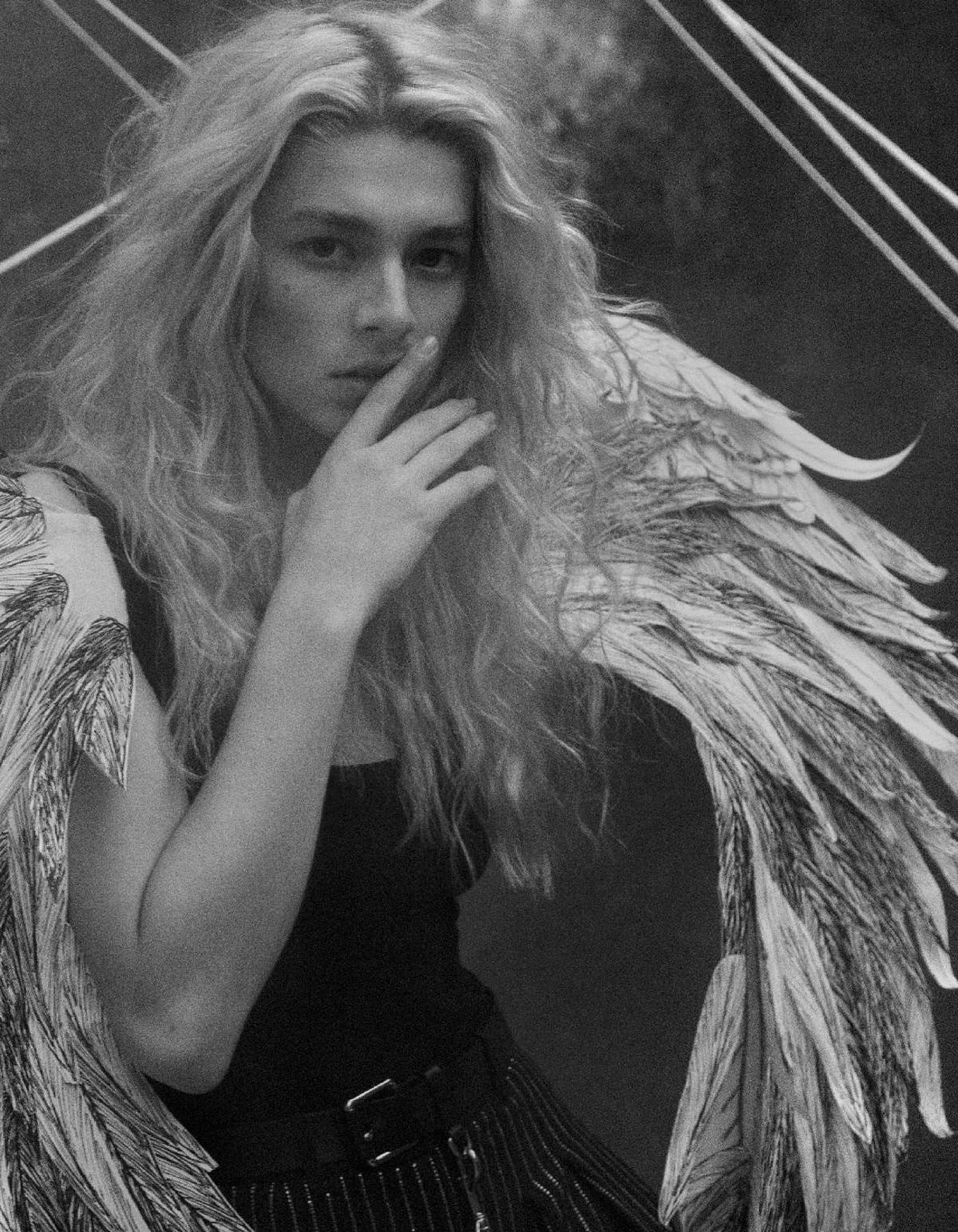 Hunter Schafer 桌布 壁紙 — 一個人的單色肖像，長髮和詳細的羽毛翅膀，手靠近嘴，在幾何背景前。