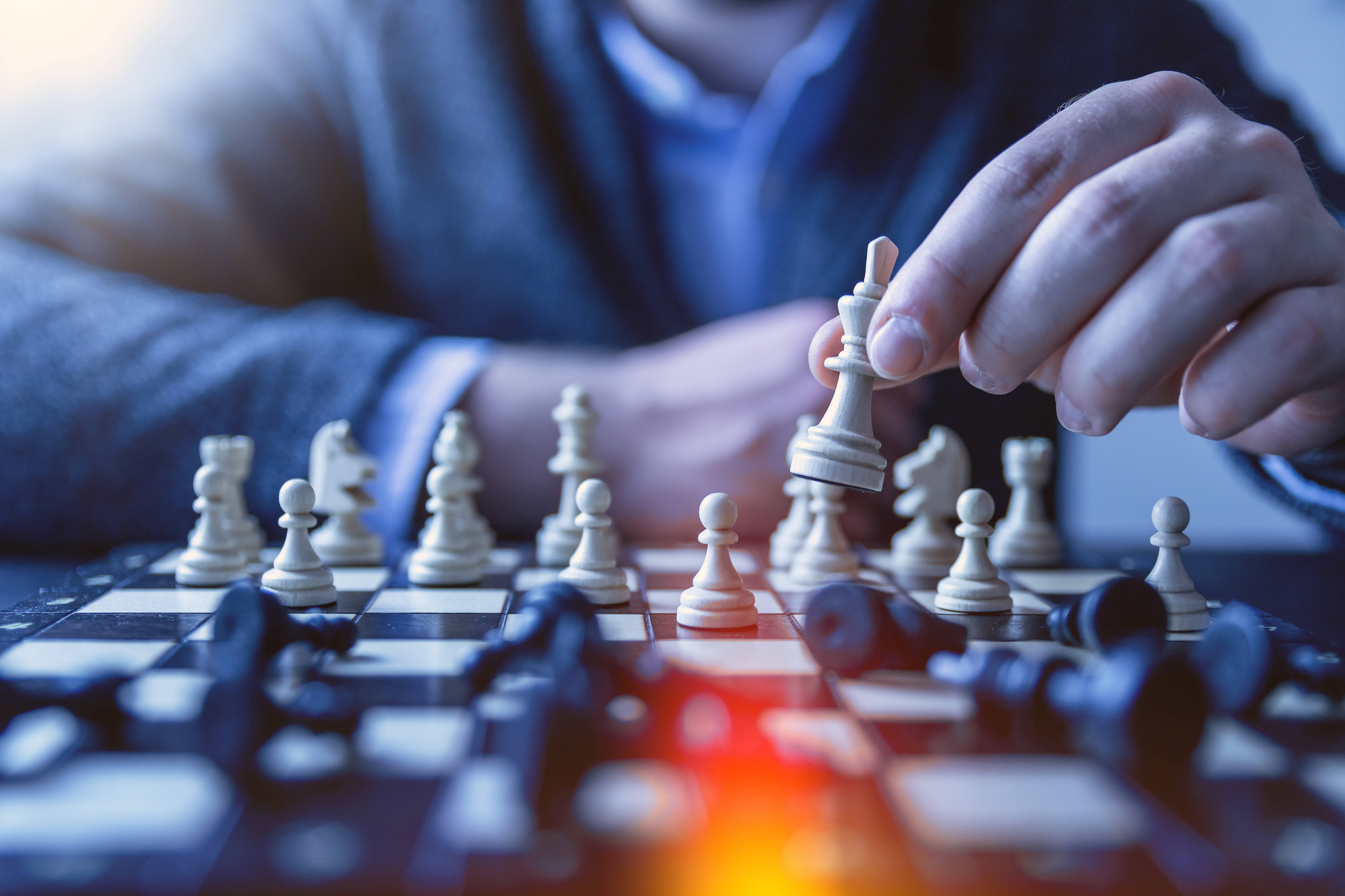 女王 桌布 壁紙 — 一個人的手在棋盤上移動西洋棋王棋，棋盤上有倒下的棋子和溫暖的光暈。
