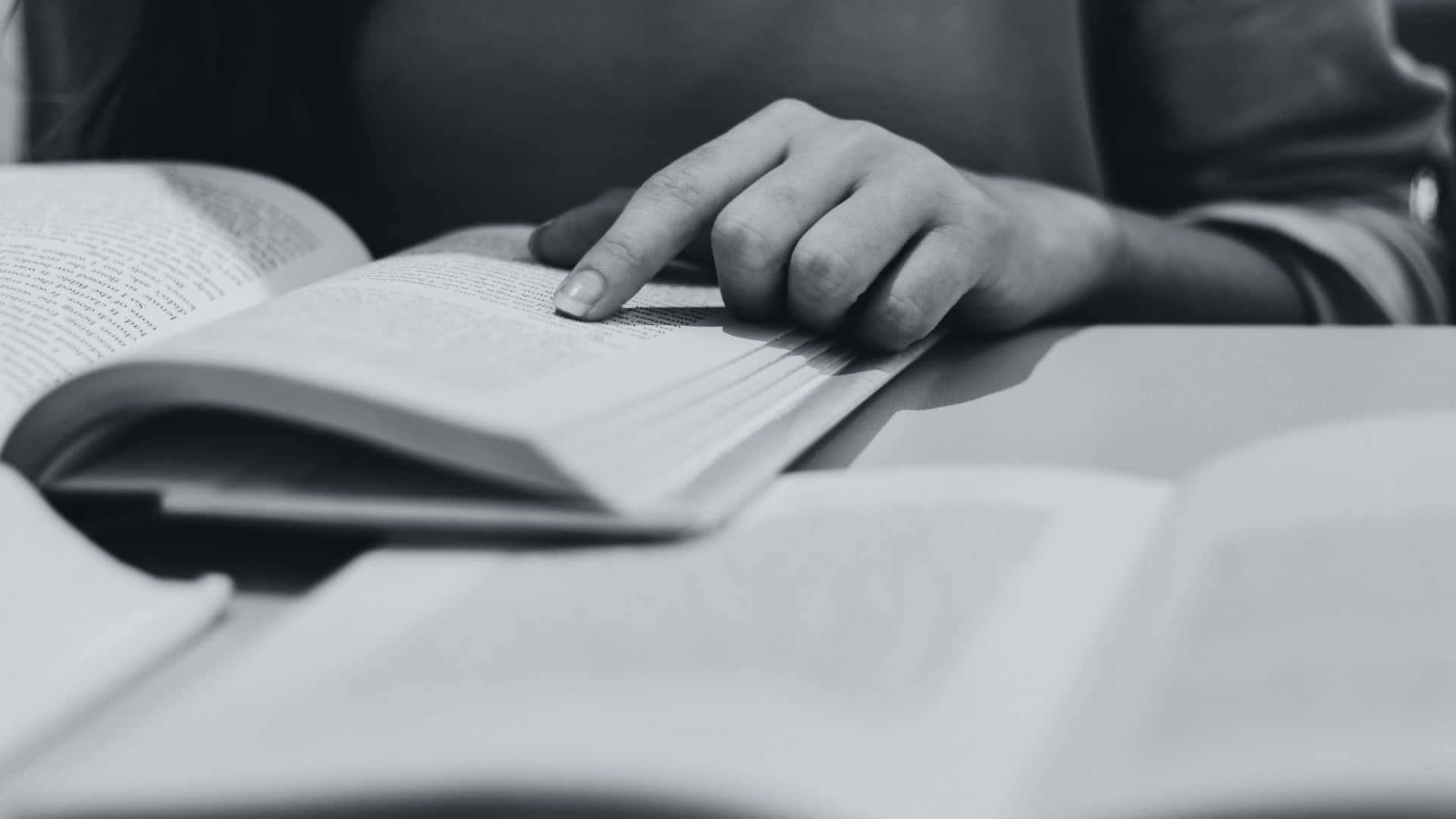 Black And White Book 桌布 壁紙 — 一個人的手在黑白特寫鏡頭中描繪一本打開的書上的文字。