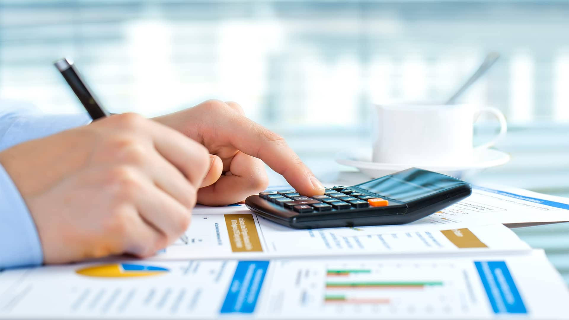 Accounting 桌布 壁紙 — 一個人的手在黑色計算機上按按鈕的特寫，計算機放在財務文件上，附近有一杯咖啡。