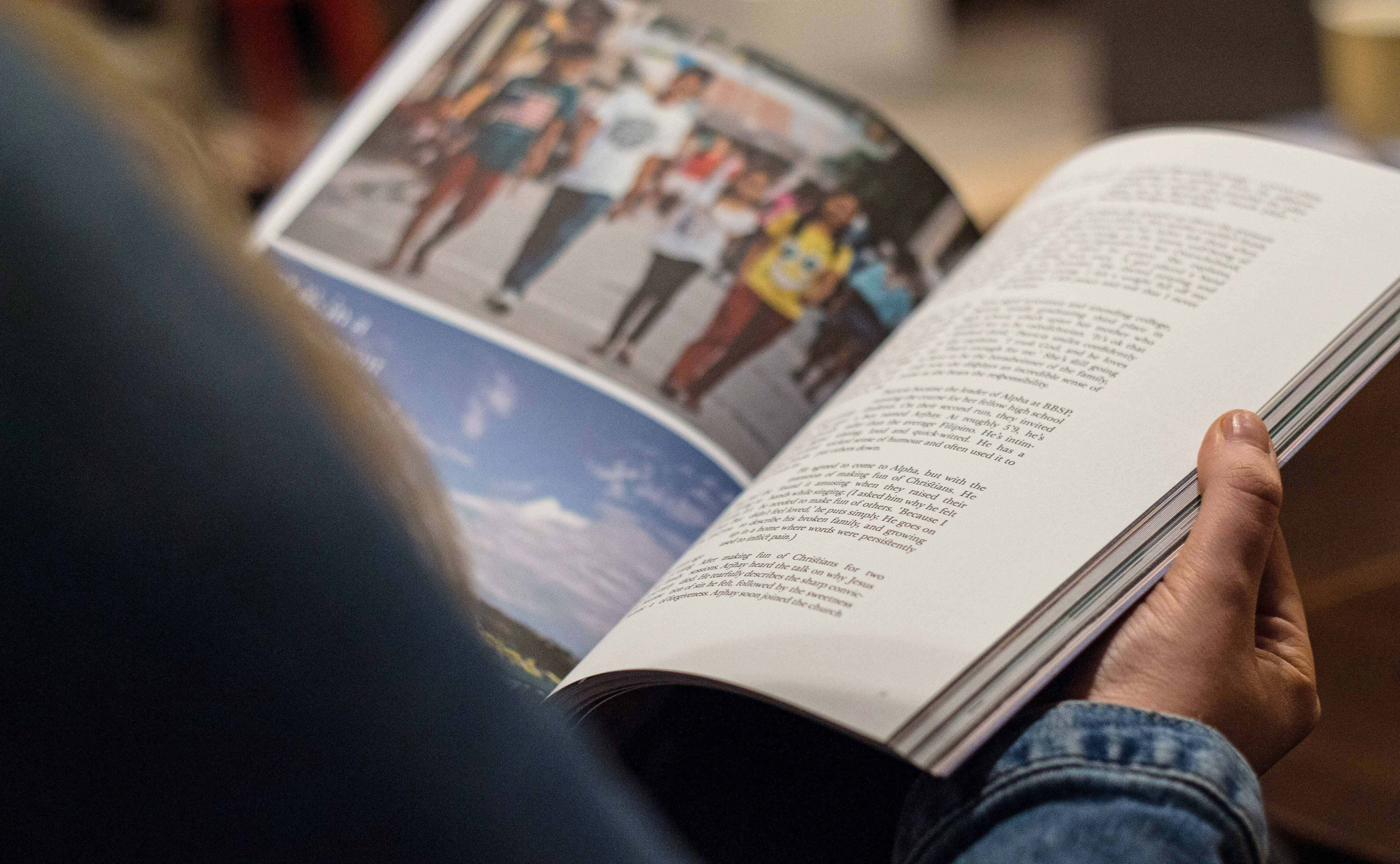 Magazine 桌布 壁紙 — 一個人的手拿著一本打開的書，其中一頁有跑步者的照片，另一頁有文字。