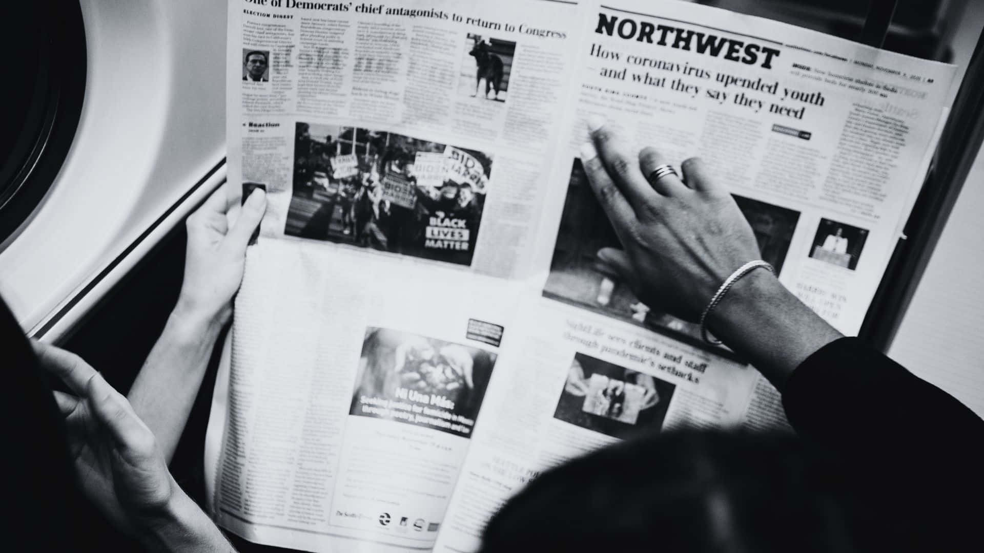 Black And White Newspaper 桌布 壁紙 — 一個人的手拿著並閱讀一份黑白報紙，上面有關於政治和社會運動的頭條新聞。