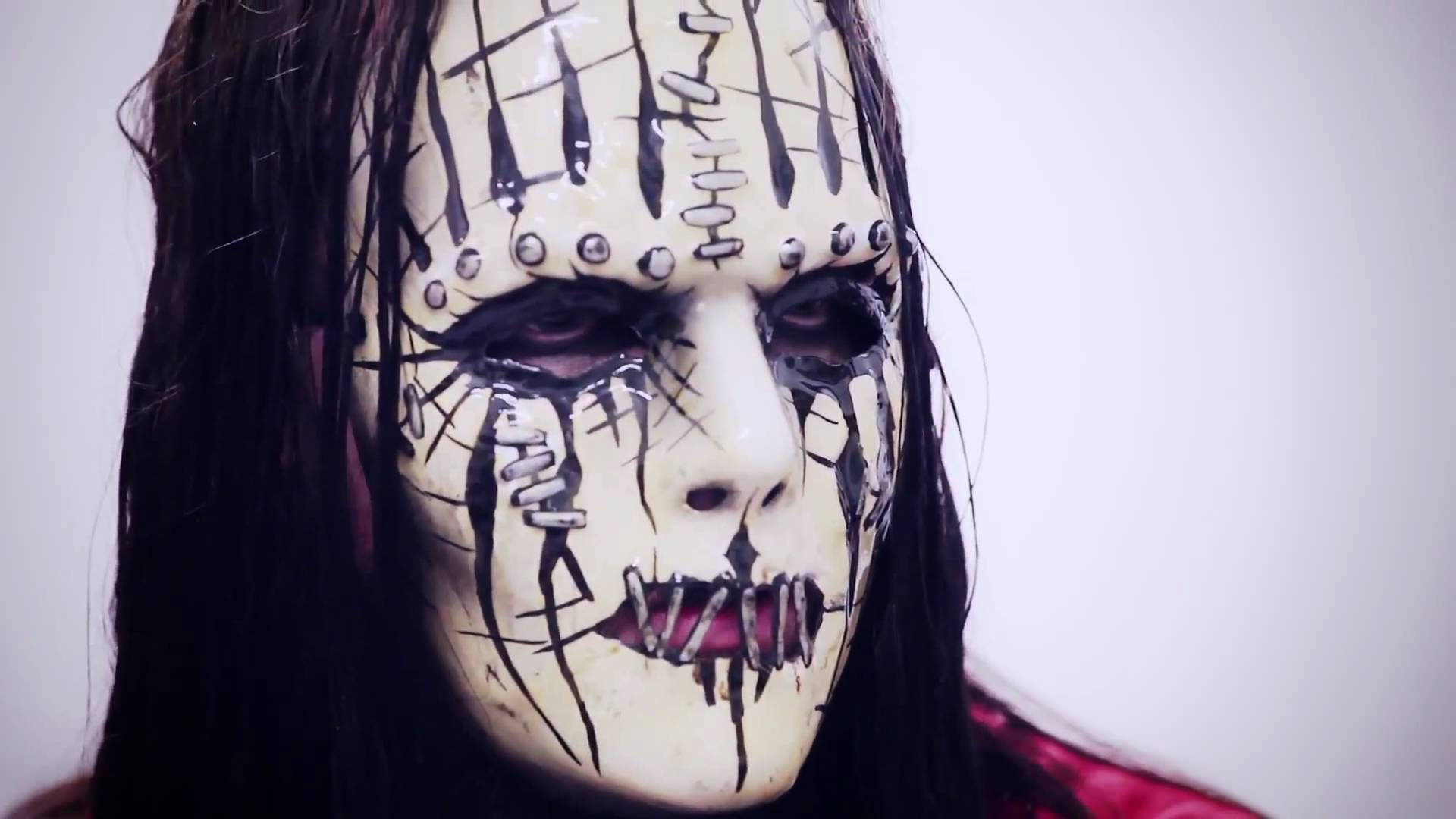 Joey Jordison 桌布 壁紙 — 一個人的特寫，戴著一個白色面具，上面有黑色縫線和金屬鉚釘，背景是純色。