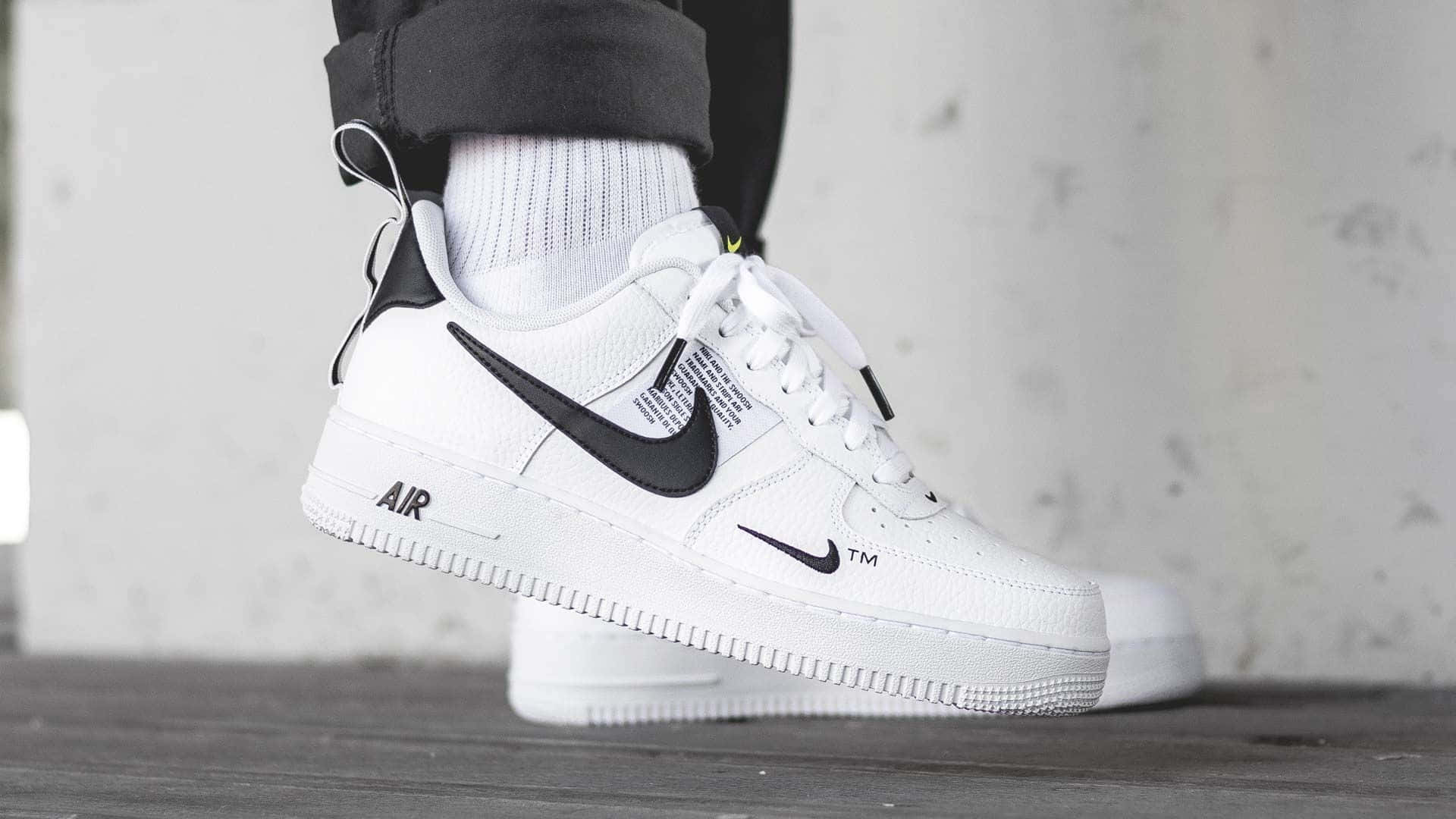 桌布 壁紙 — 一個人的特寫，穿著白色Nike Air Force 1運動鞋搭配黑色點綴和羅紋襪，背景是有紋理的灰色牆壁。