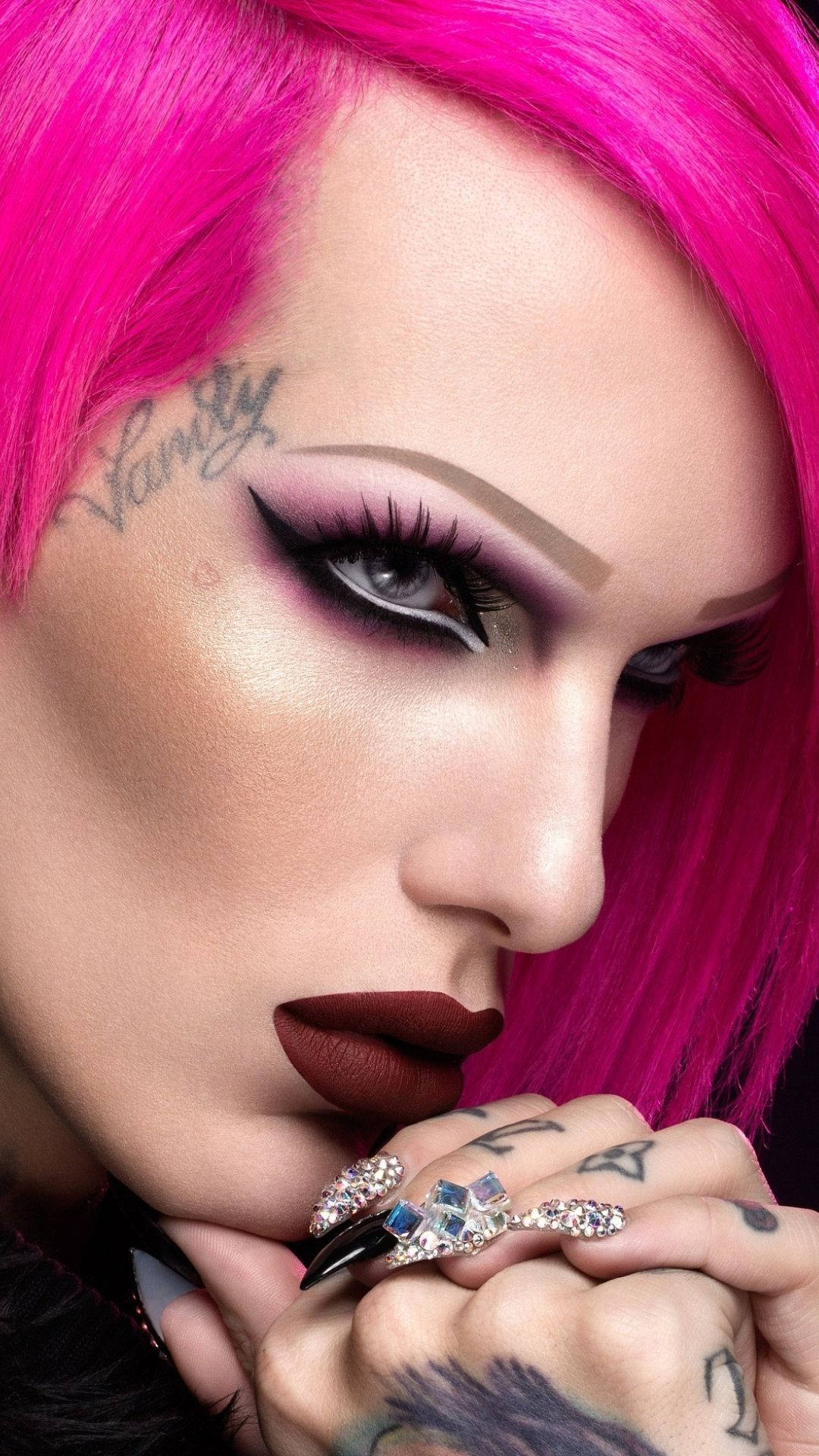 Jeffree Star 桌布 壁紙 — 一個人的特寫肖像，擁有充滿活力的粉紅色頭髮、大膽的化妝和紋身，帶著鑲有寶石的指甲凝視著。