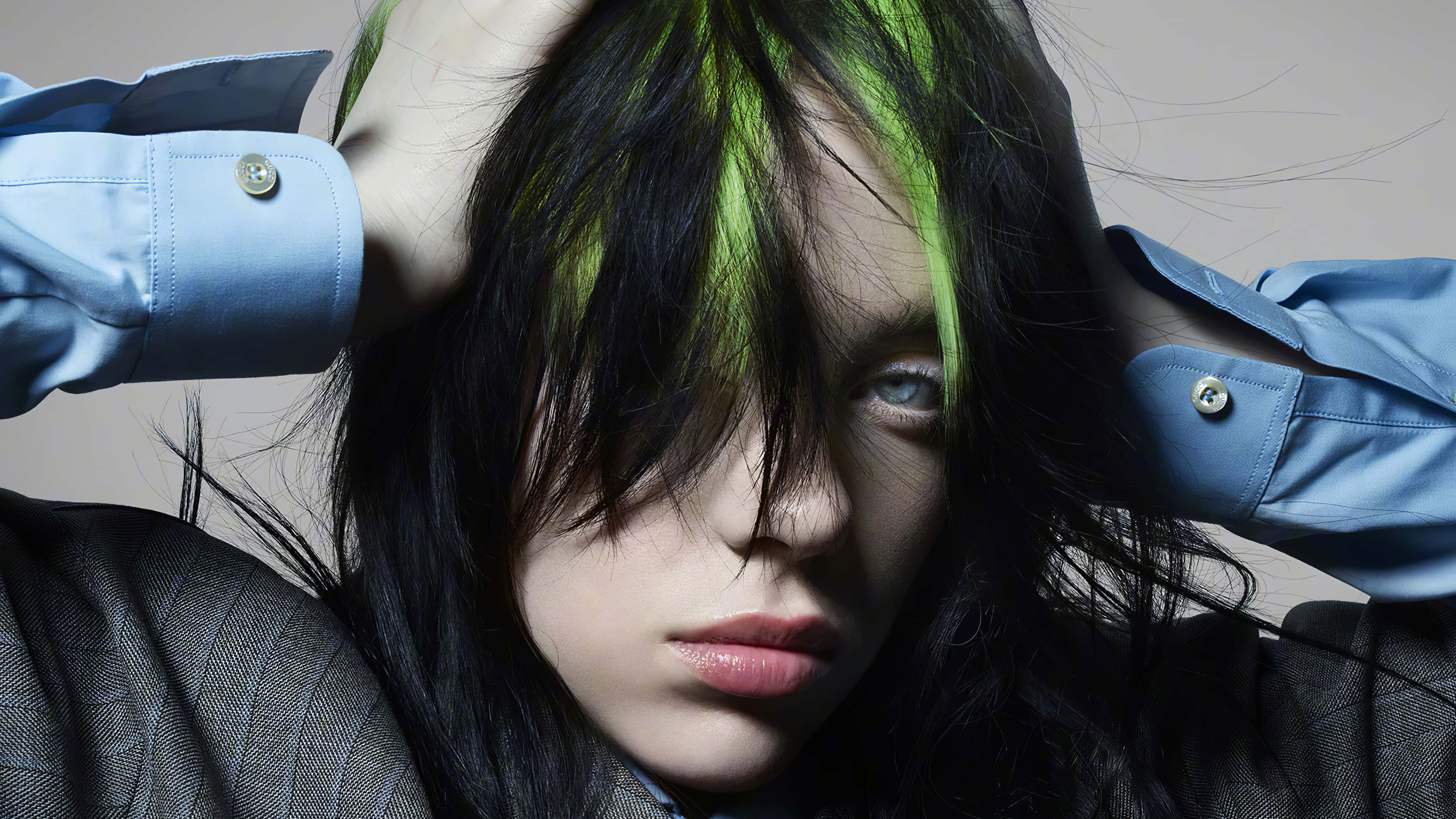 Billie Eilish Laptop 桌布 壁紙 — 一個人的特寫肖像，深色頭髮上有引人注目的綠色條紋，雙手抓著頭部，穿著藍色襯衫和灰色西裝外套。