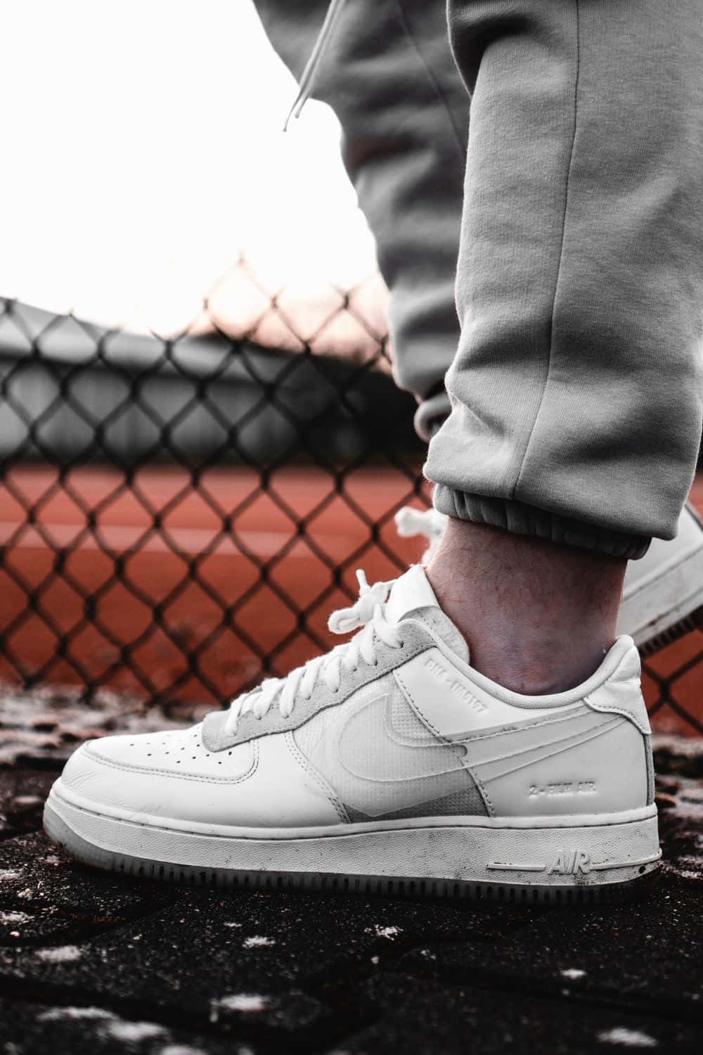 鞋子 桌布 壁紙 — 一個人的白色Nike Air Force 1運動鞋在濕漉漉的人行道上靠近鐵絲網圍欄的特寫。
