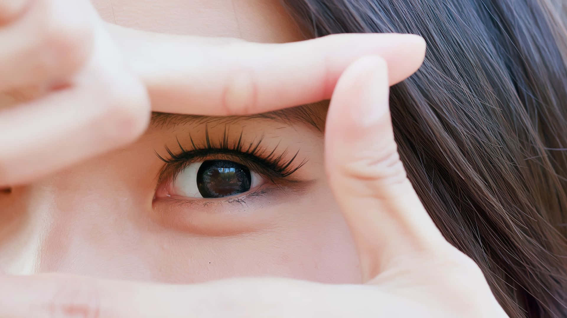 Eye 桌布 壁紙 — 一個人的眼睛特寫，手指形成一個小矩形框住眼睛，背景是柔軟的皮膚和深色頭髮。