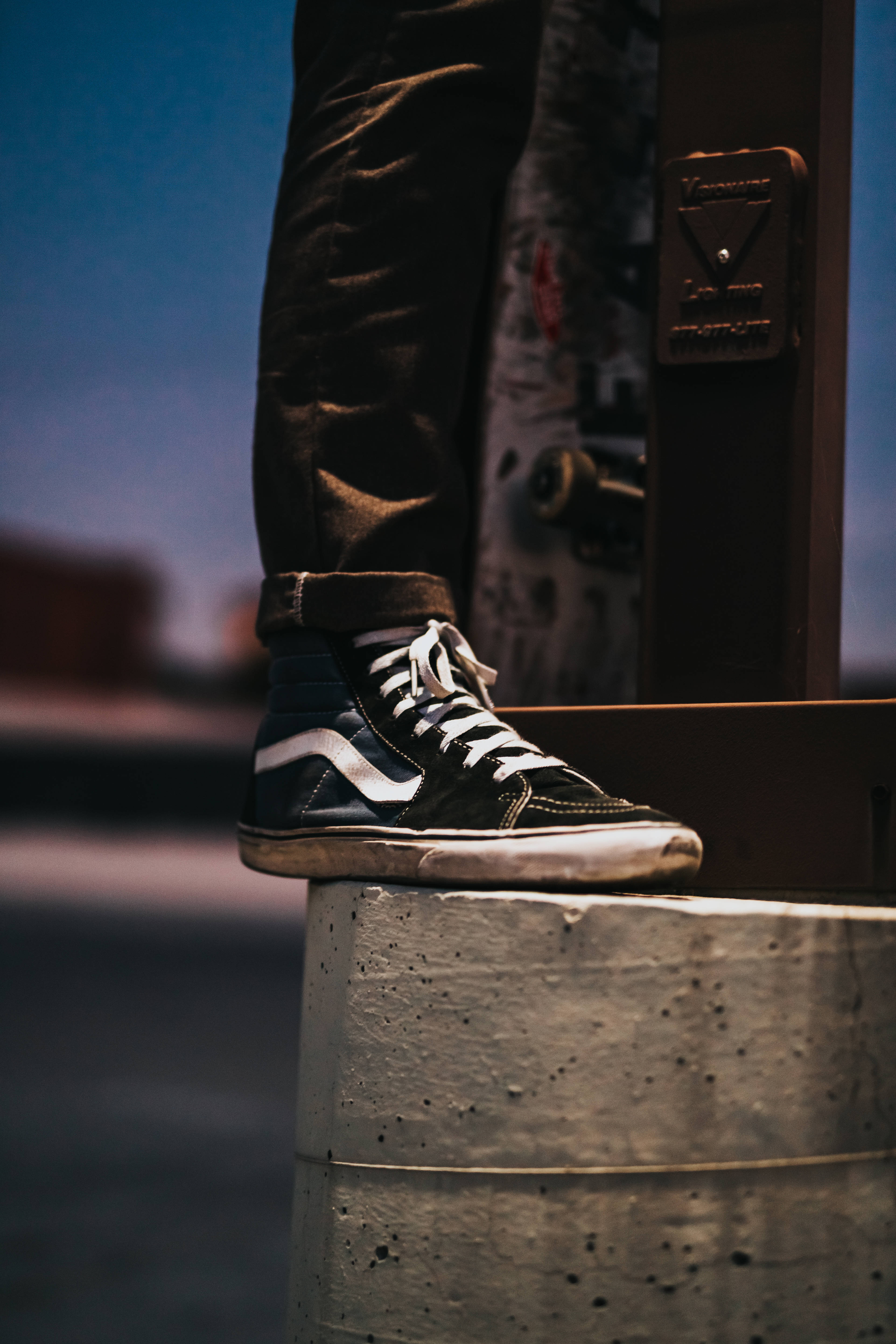 Vans 桌布 壁紙 — 一個人的磨損黑色Vans運動鞋的特寫，棲息在混凝土柱上，背景是暮色城市。