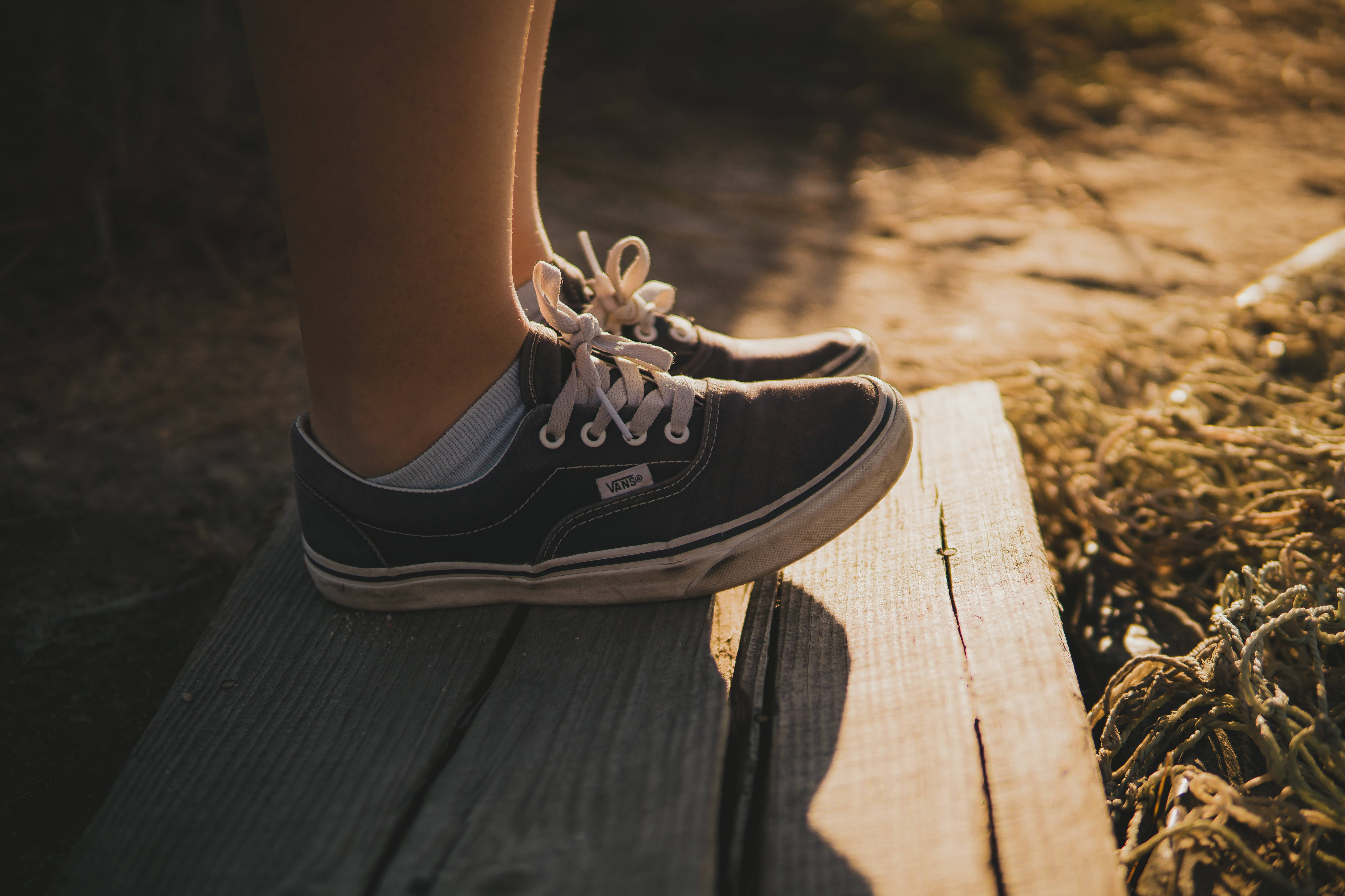 Vans 桌布 壁紙 — 一個人的腳穿著深色Vans運動鞋，擱在經風化的木板上，沐浴在溫暖的金色陽光中。