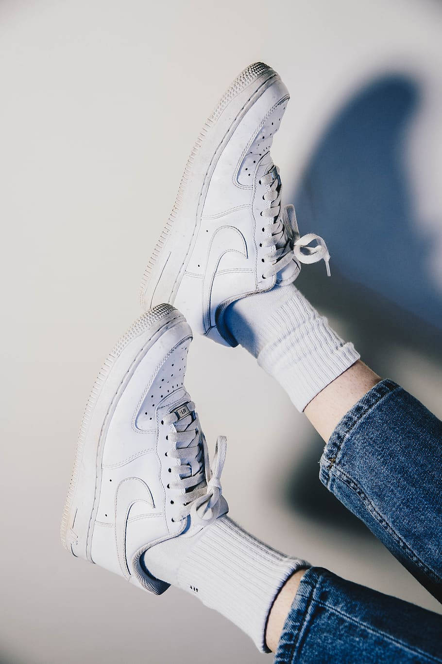 Nike Shoes 桌布 壁紙 — 一個人的腳穿著白色Nike運動鞋和羅紋襪子，隨意地靠在一面帶有柔和陰影的素牆上。
