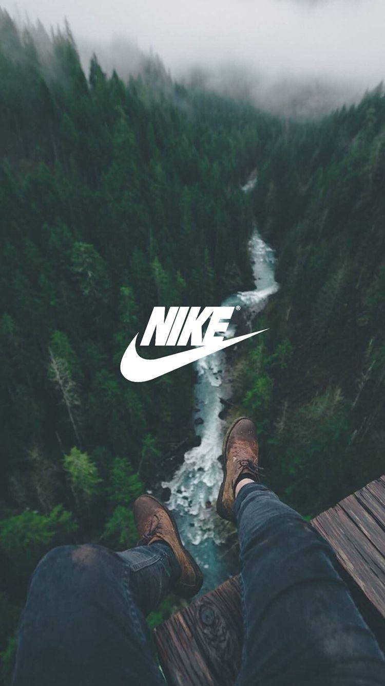 Nike iPhone 桌布 壁紙 — 一個人的腳穿著靴子懸掛在木製平台上，俯瞰著霧氣瀰漫的森林峽谷，下方有湍急的河流。