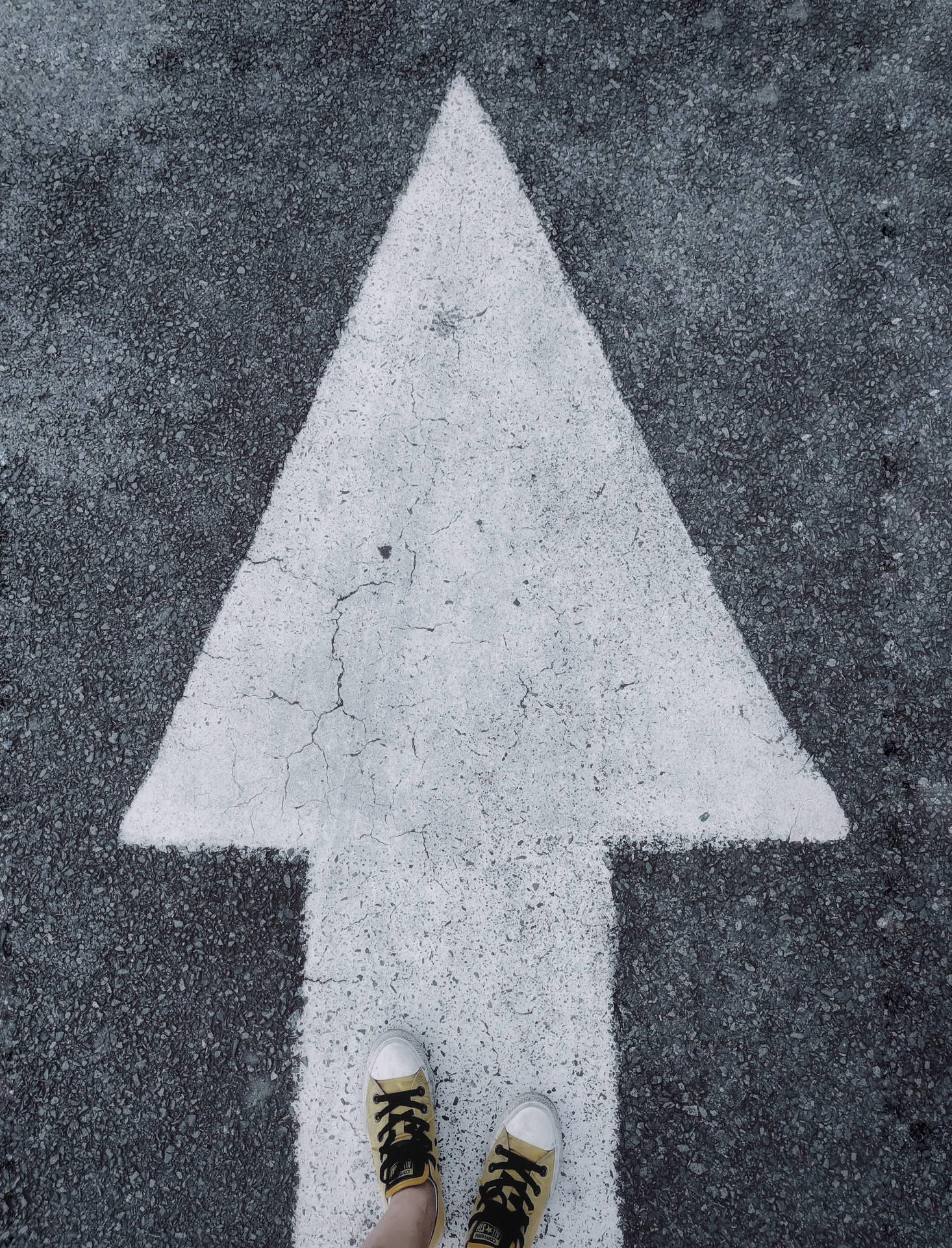 穿著黃色運動鞋的腳站在瀝青上繪製的一個大型白色箭頭上。 — 鞋子 GIF 壁紙