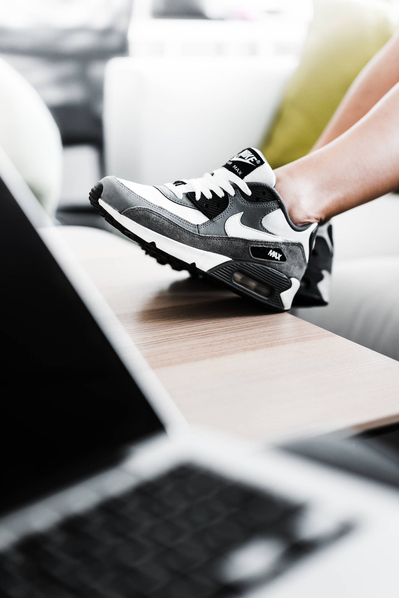 鞋子 桌布 壁紙 — 一個人的腳穿著黑白Nike Air Max運動鞋，擱在現代客廳的木桌上，旁邊放著一台打開的筆記型電腦。