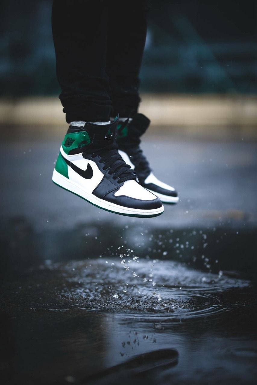 Nike Air Jordan 1 桌布 壁紙 — 一個人的腳穿著黑白綠色的運動鞋，在雨水浸濕的人行道上跳躍，濺起水花。