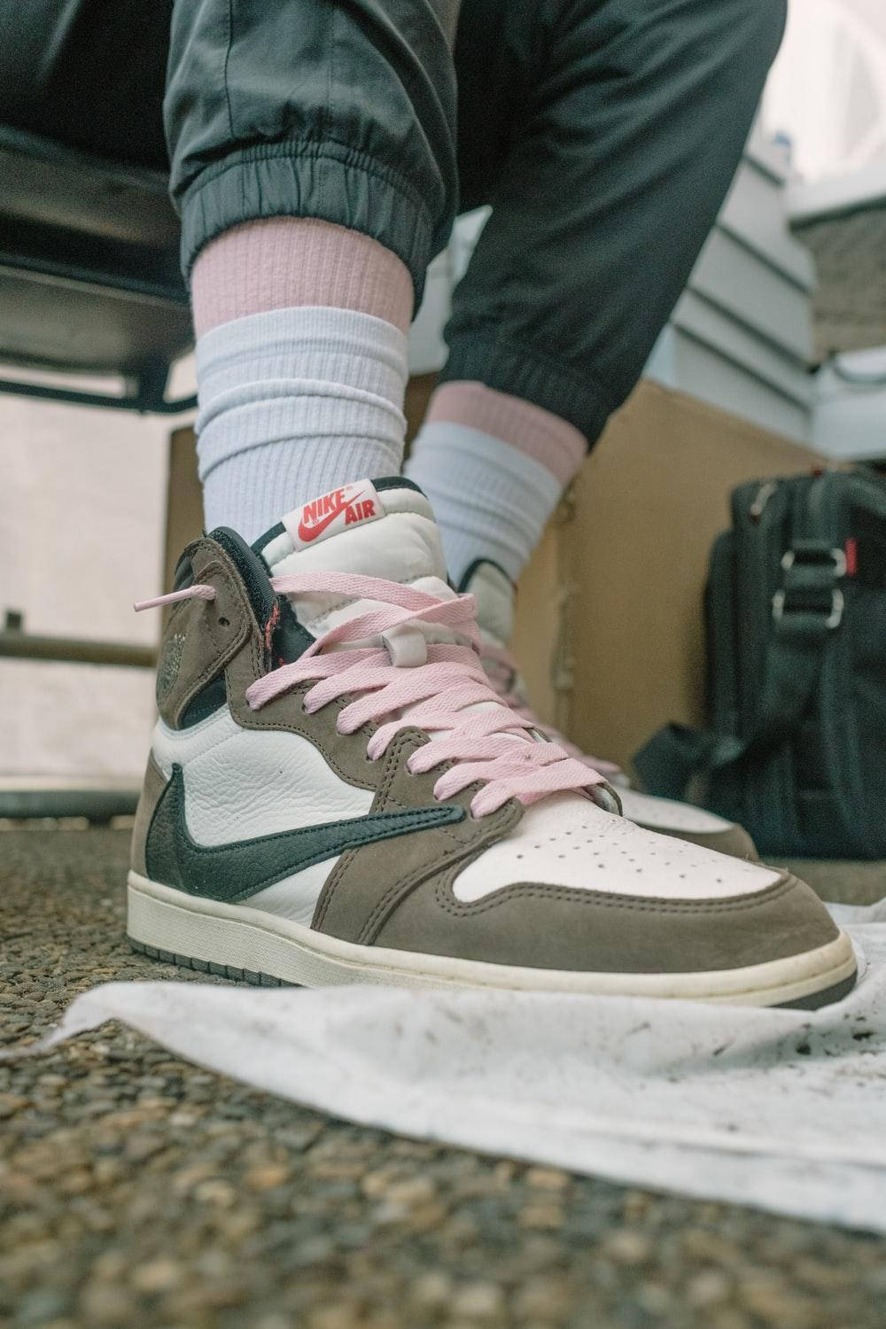 崔維斯·史考特 桌布 壁紙 — 一個人的腳部特寫，穿著灰色和白色Nike Air運動鞋，粉紅色鞋帶，擱在碎石表面上。