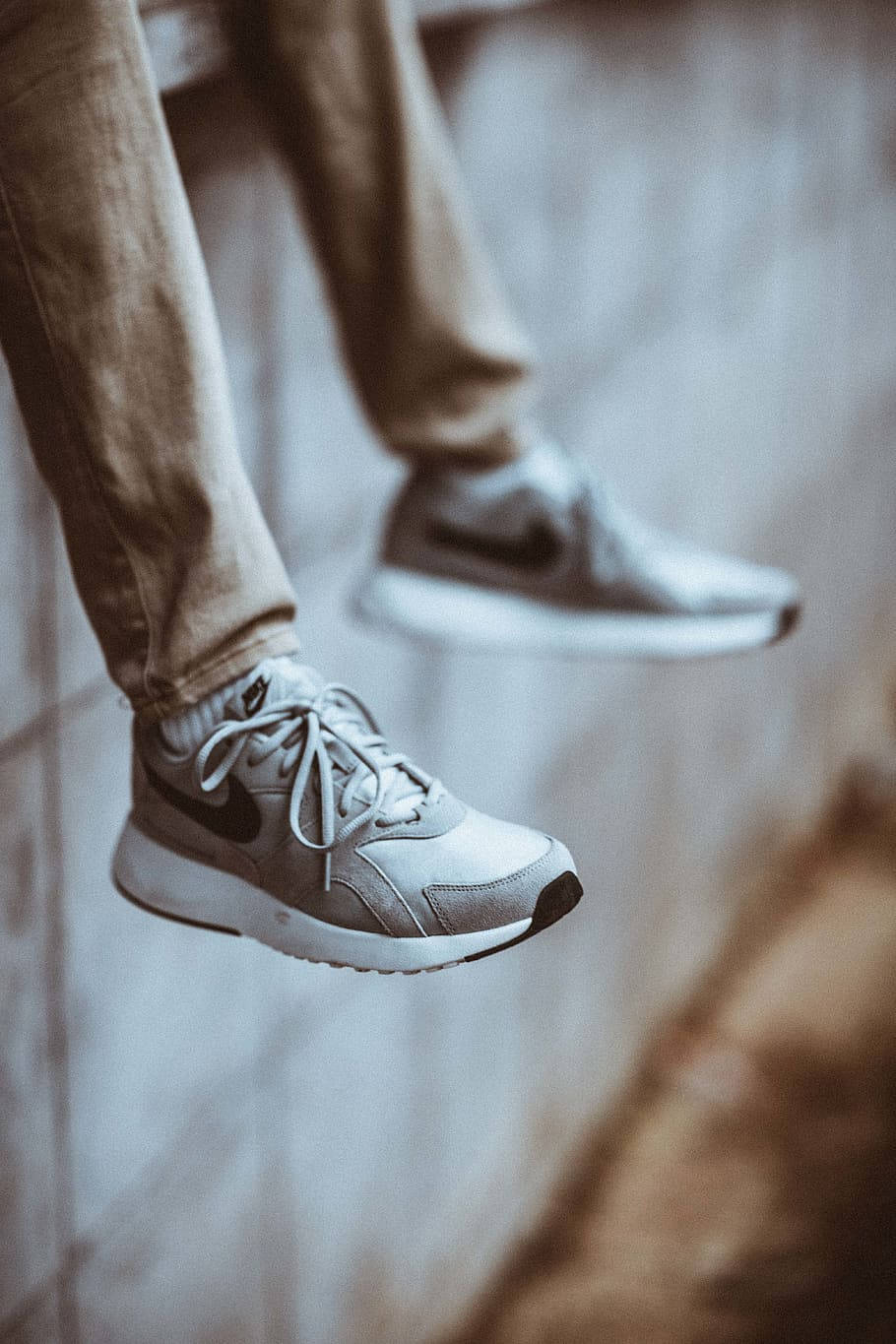 Nike Shoes 桌布 壁紙 — 一個人的腳部特寫，穿著灰色運動鞋，隨意地懸掛在模糊的混凝土牆前。