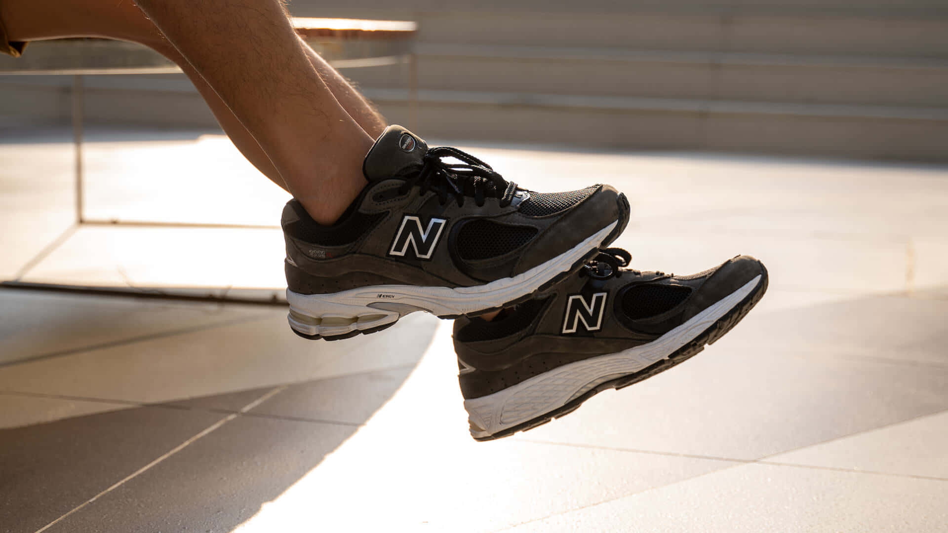 New Balance 桌布 壁紙 — 一個人的腿穿著黑色New Balance運動鞋，在陽光照射的混凝土台階上方騰空。