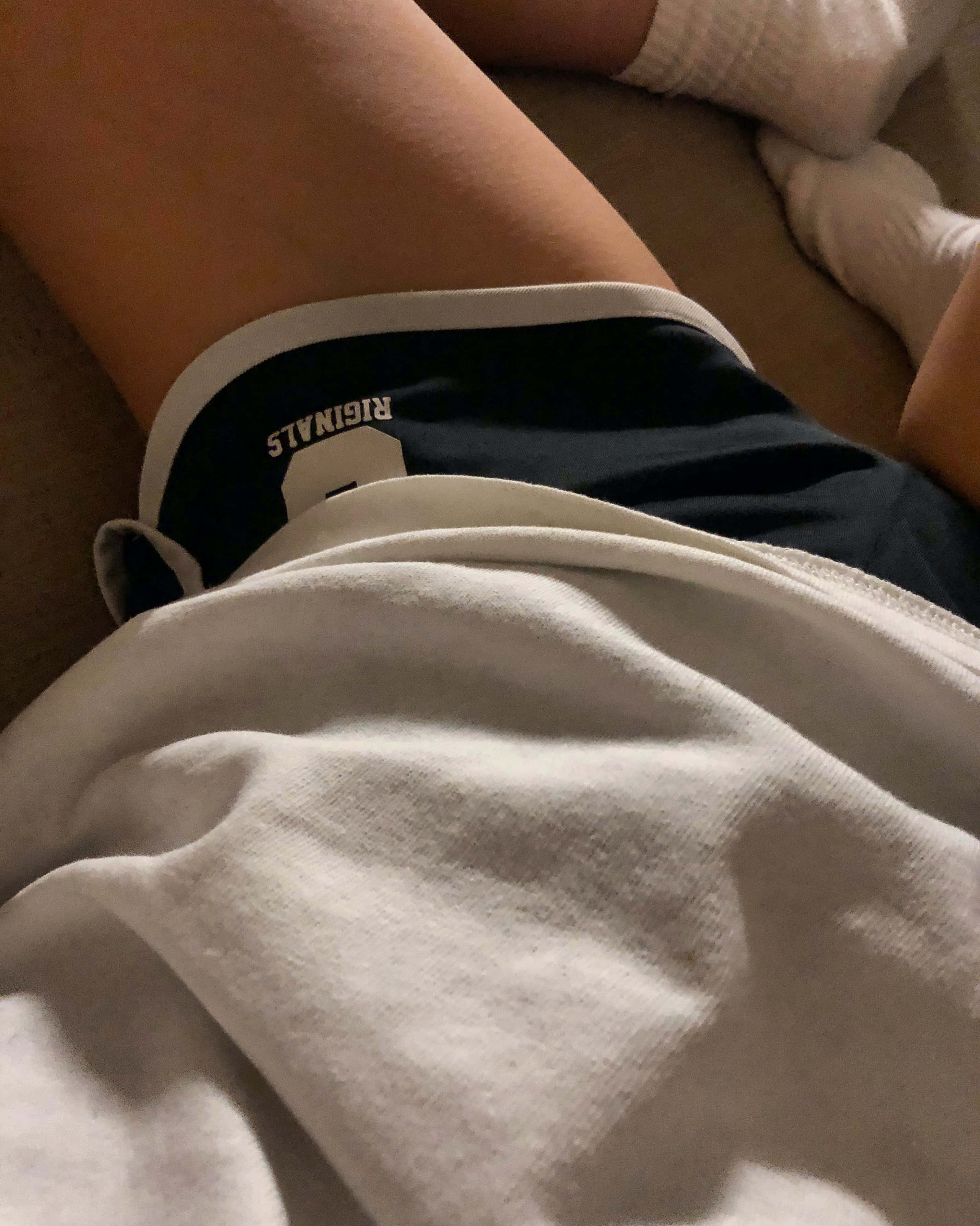 Athletic 桌布 壁紙 — 一個人的腿部特寫，穿著白色襪子和深色短褲（有白色邊），在米色沙發上休息。