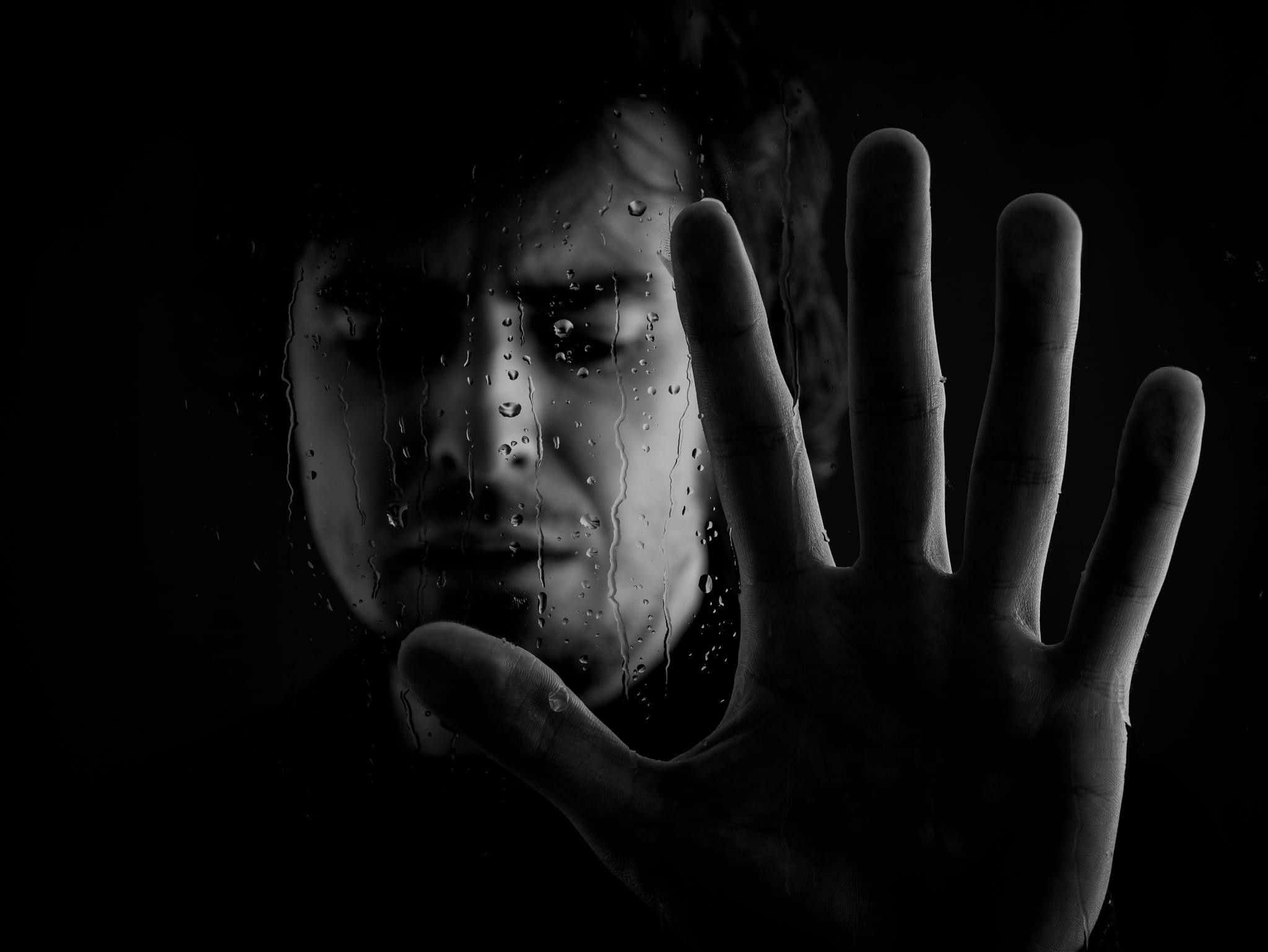 Dark Emotional 桌布 壁紙 — 一個人的臉和手壓在雨水濕滑的窗戶上，以強烈的黑白對比傳達孤立和渴望。